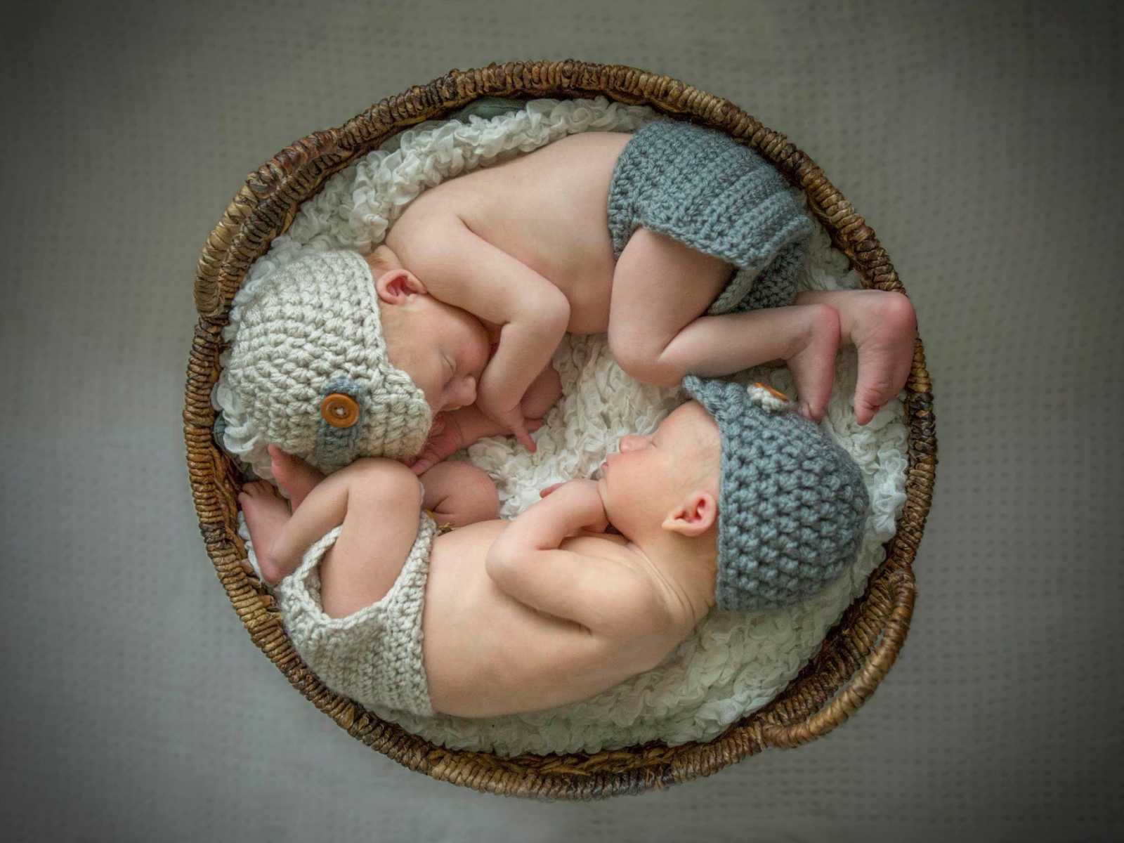 newborn twins curled up in basket with knit diaper and hat on