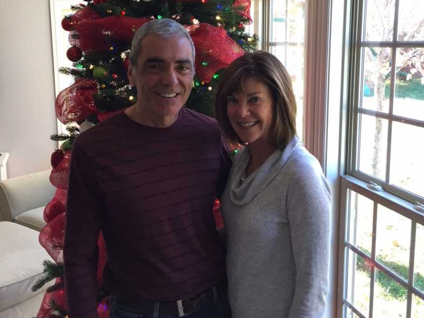 husband and wife posing in front of christmas tree