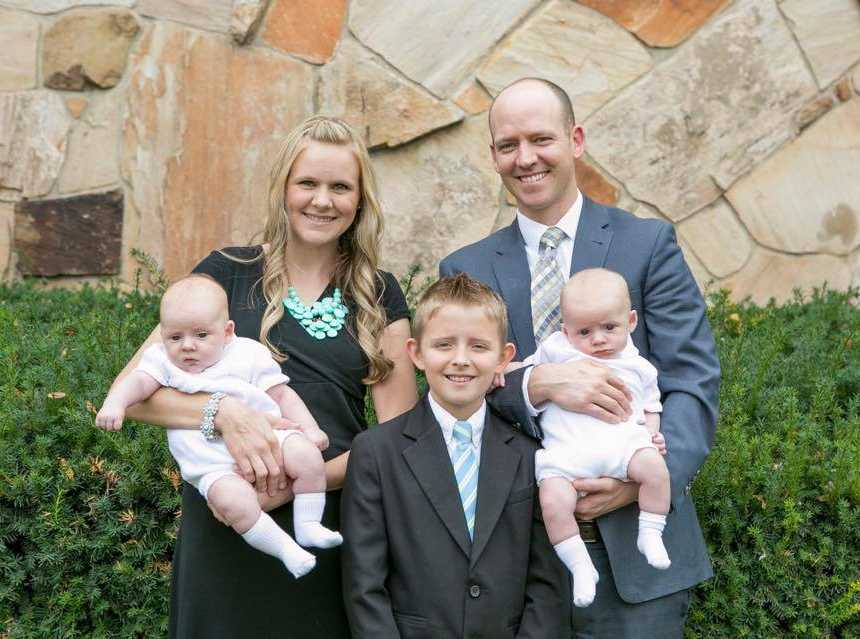 mother and father smile while holding babies in their arms with older son smiling in the middle of them