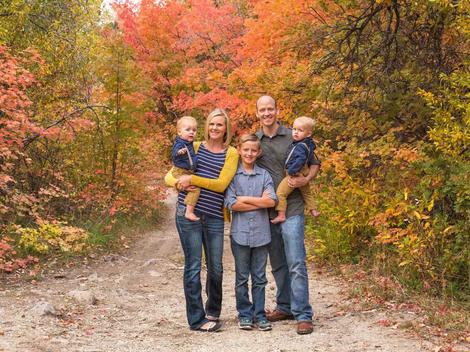 mother and father holding infant twins in the woods with older son in the middle of them