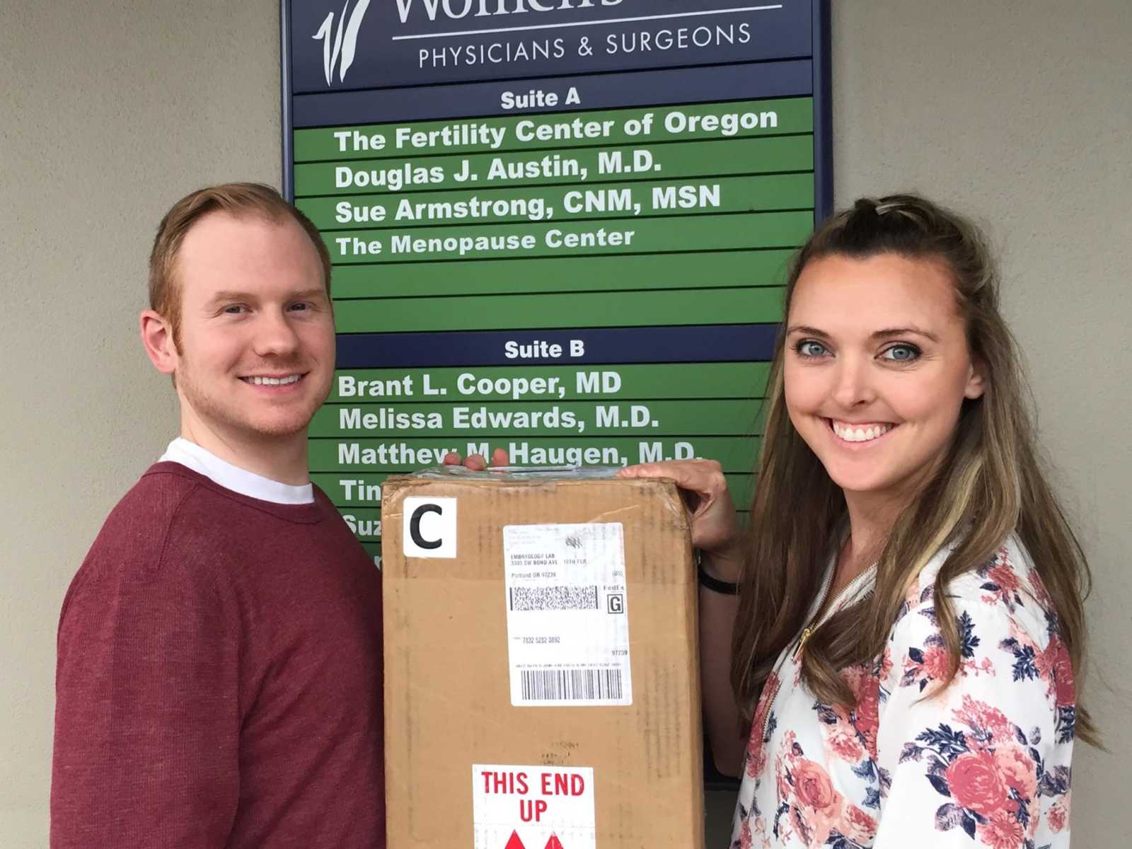 man and woman holding a shipment box of embryos in front of a sign that reads, "The Fertility Center of Oregon"