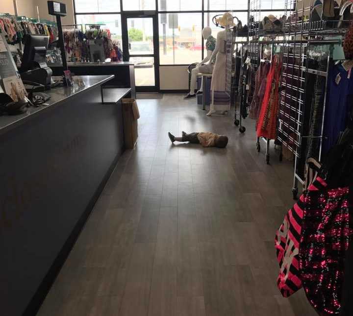 Toddler lies on his back on floor of clothing store