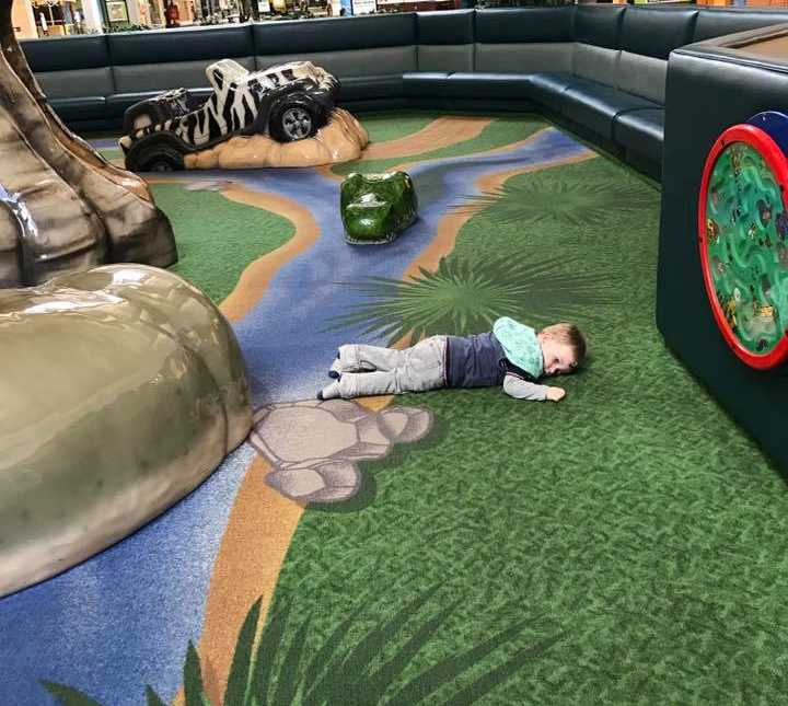 Toddler lies on his stomach in children's play place in mall