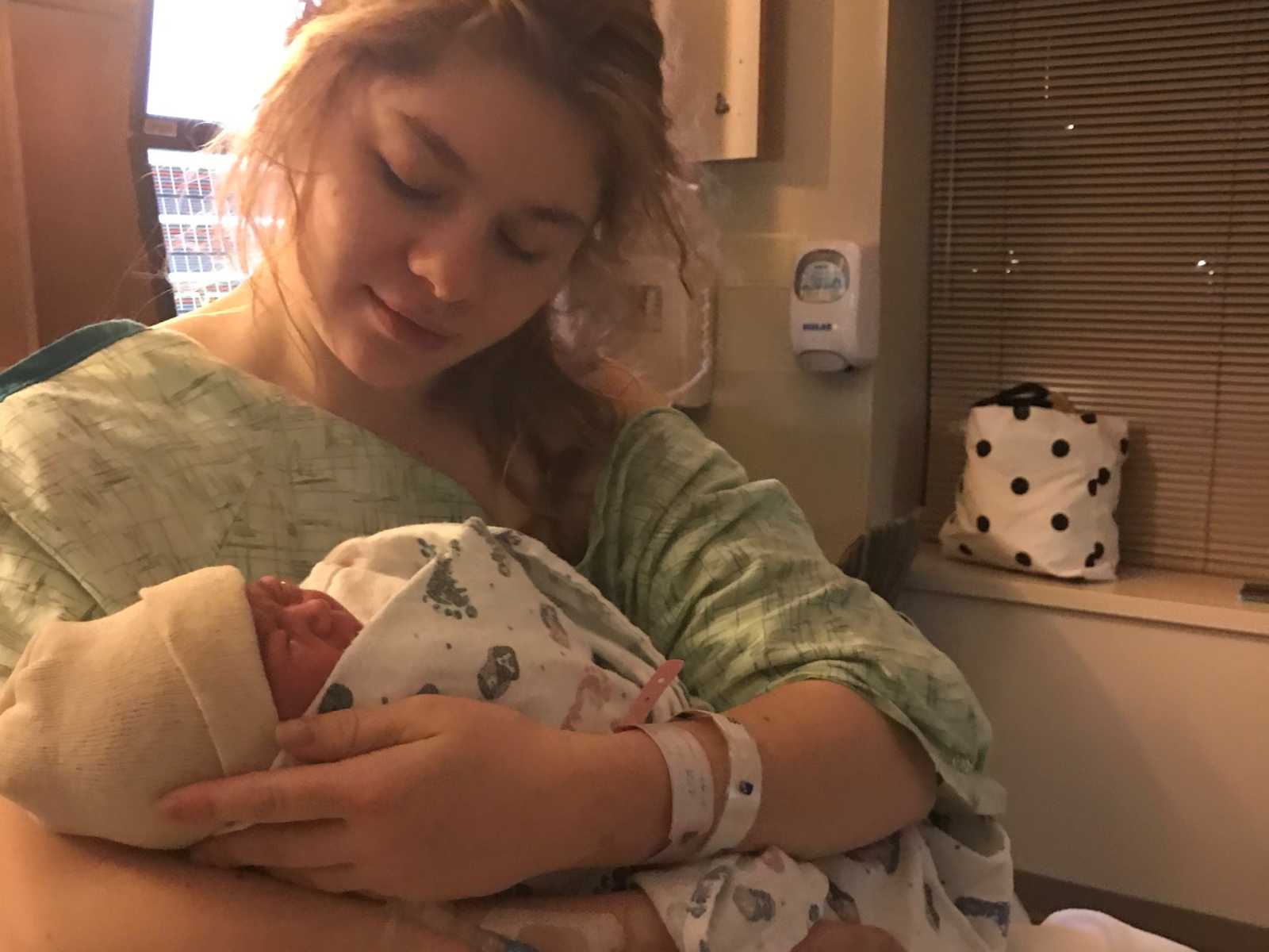 mother holds newborn baby in hospital gown