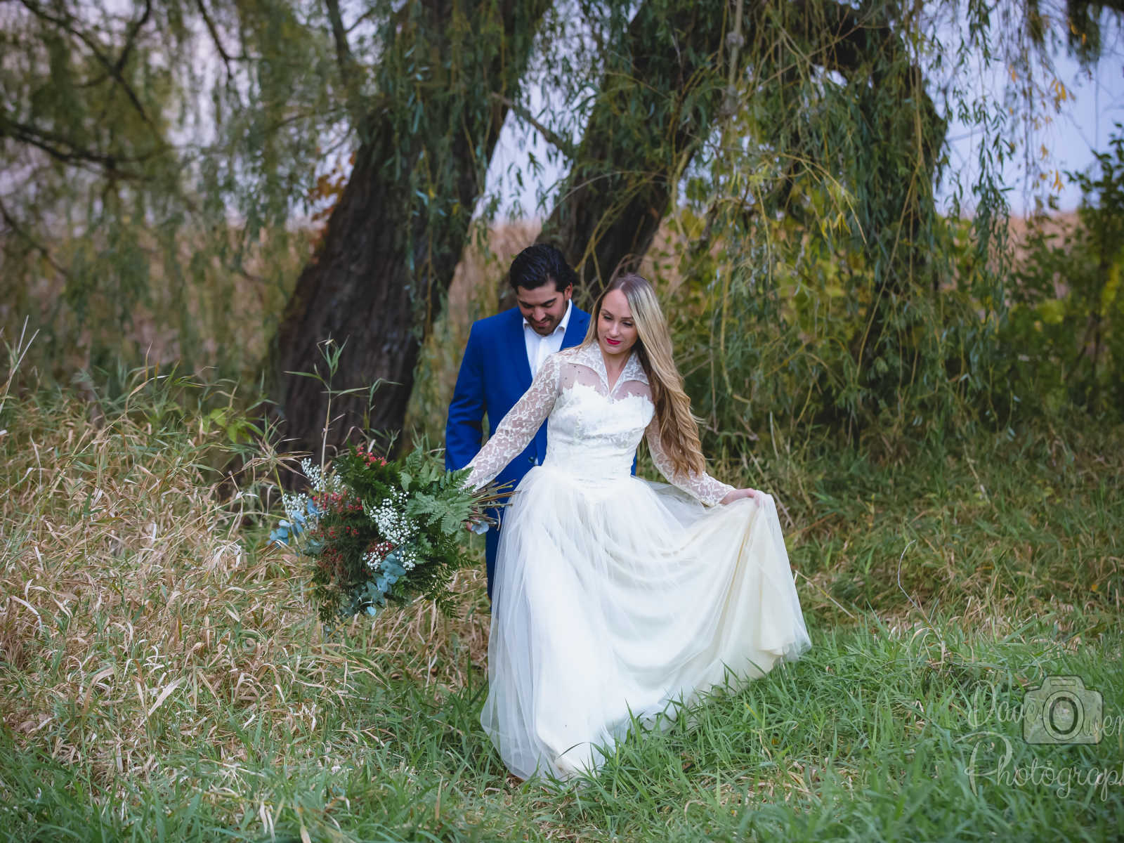 engaged couple in white dress and blue suit embrace in grass