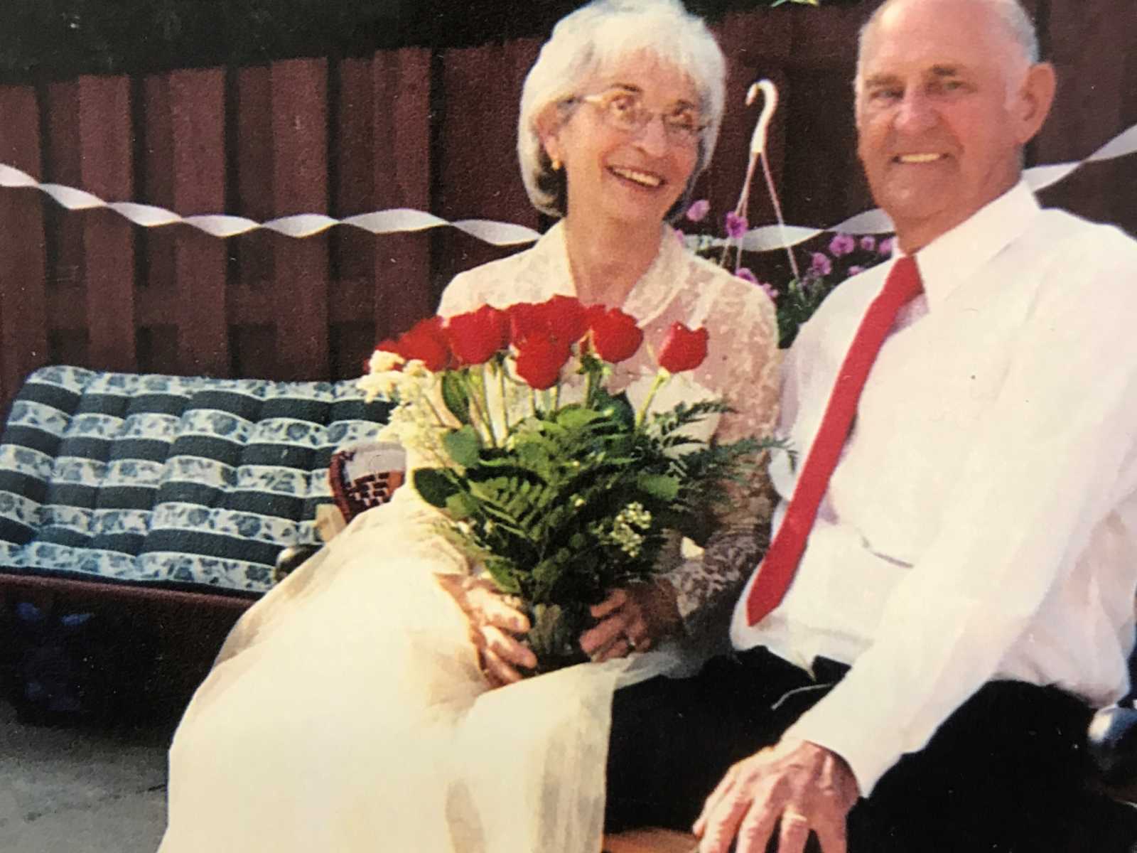 married couple sitting in formal attire with red roses in wifes lap