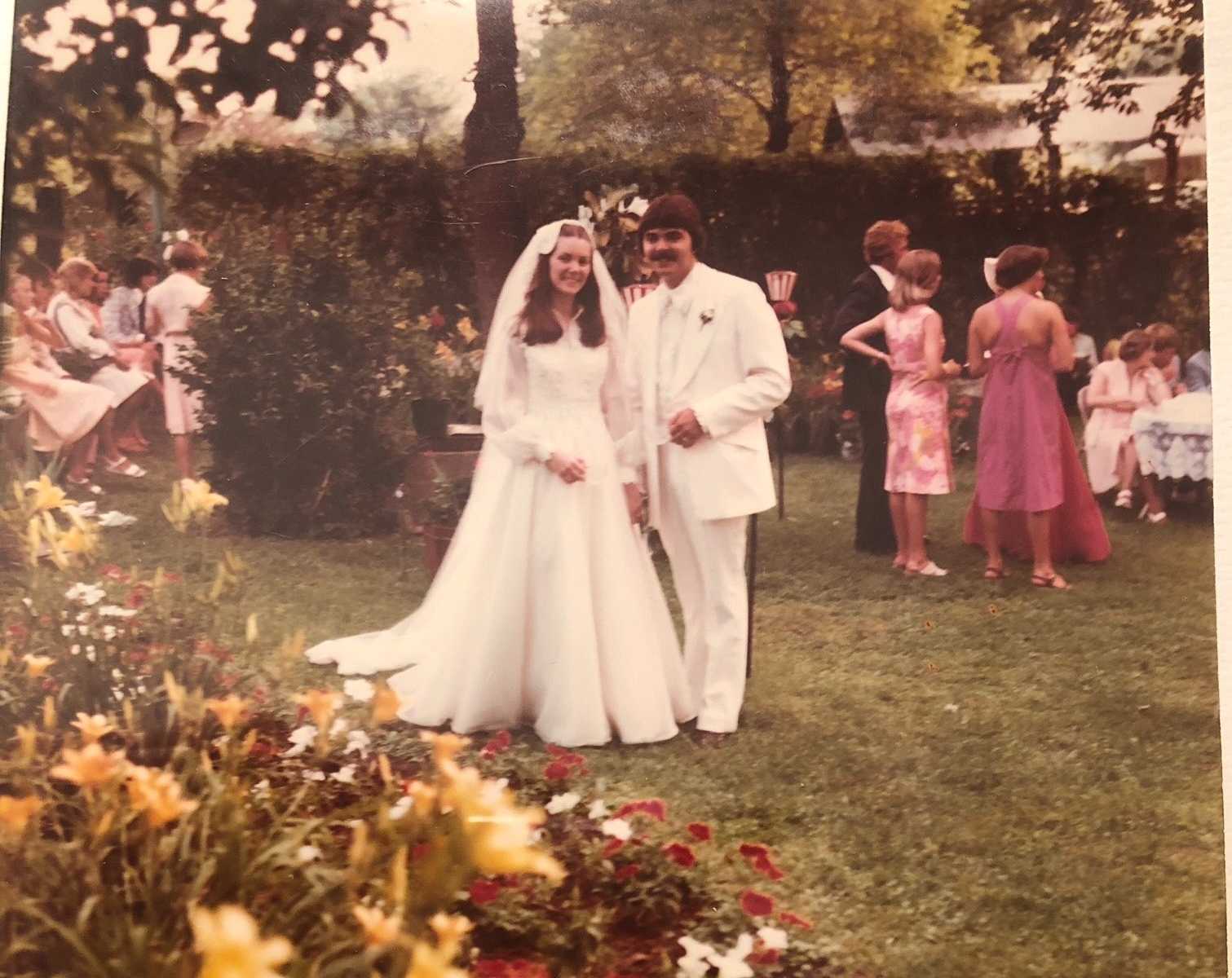 married couple at their wedding in yard with guests in the backgrounf