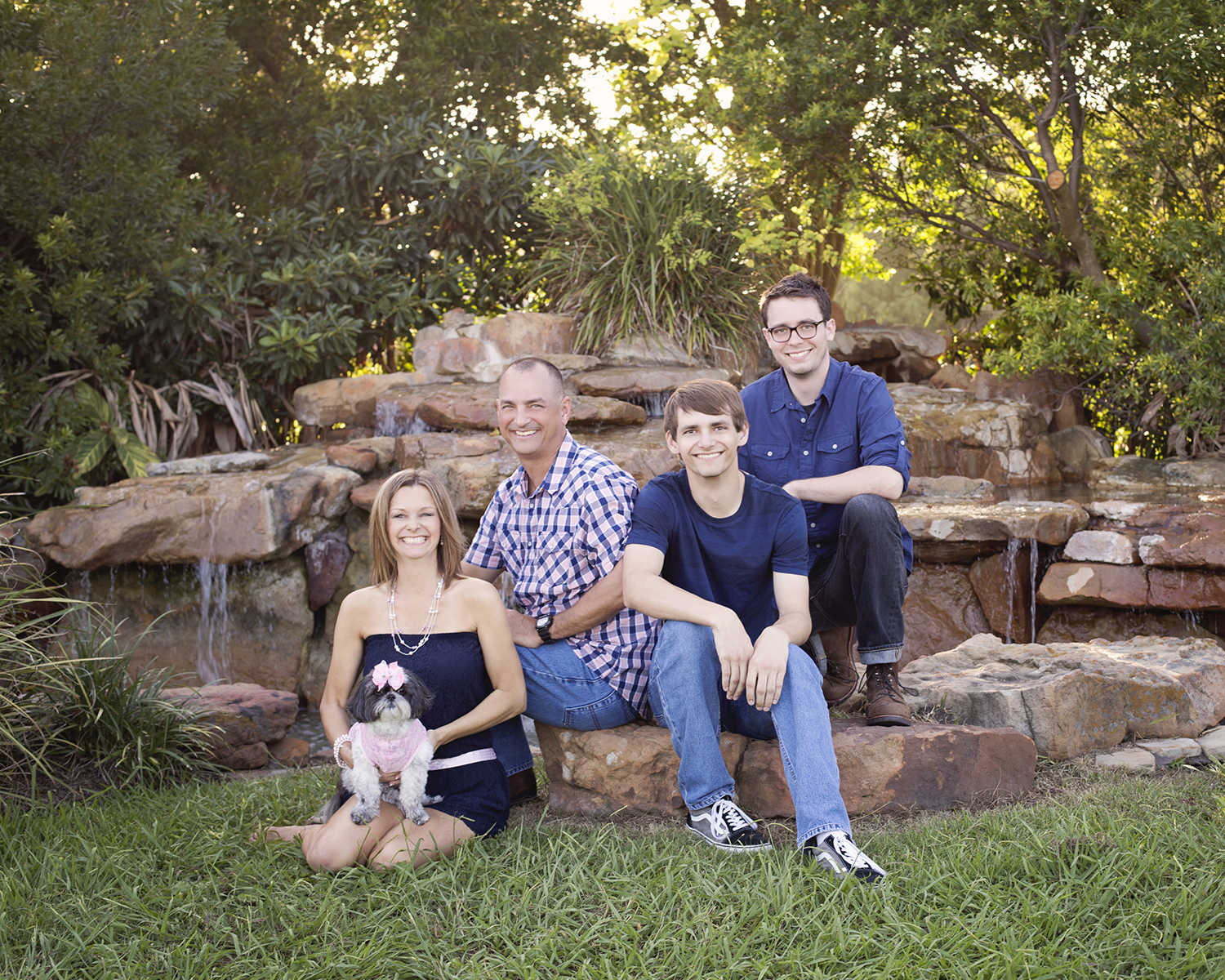 husband and wife sitting on stones with their two sons and dog smiling