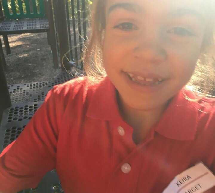 young girl with terminal illness wearing red collared shirt and target name tag smiles 