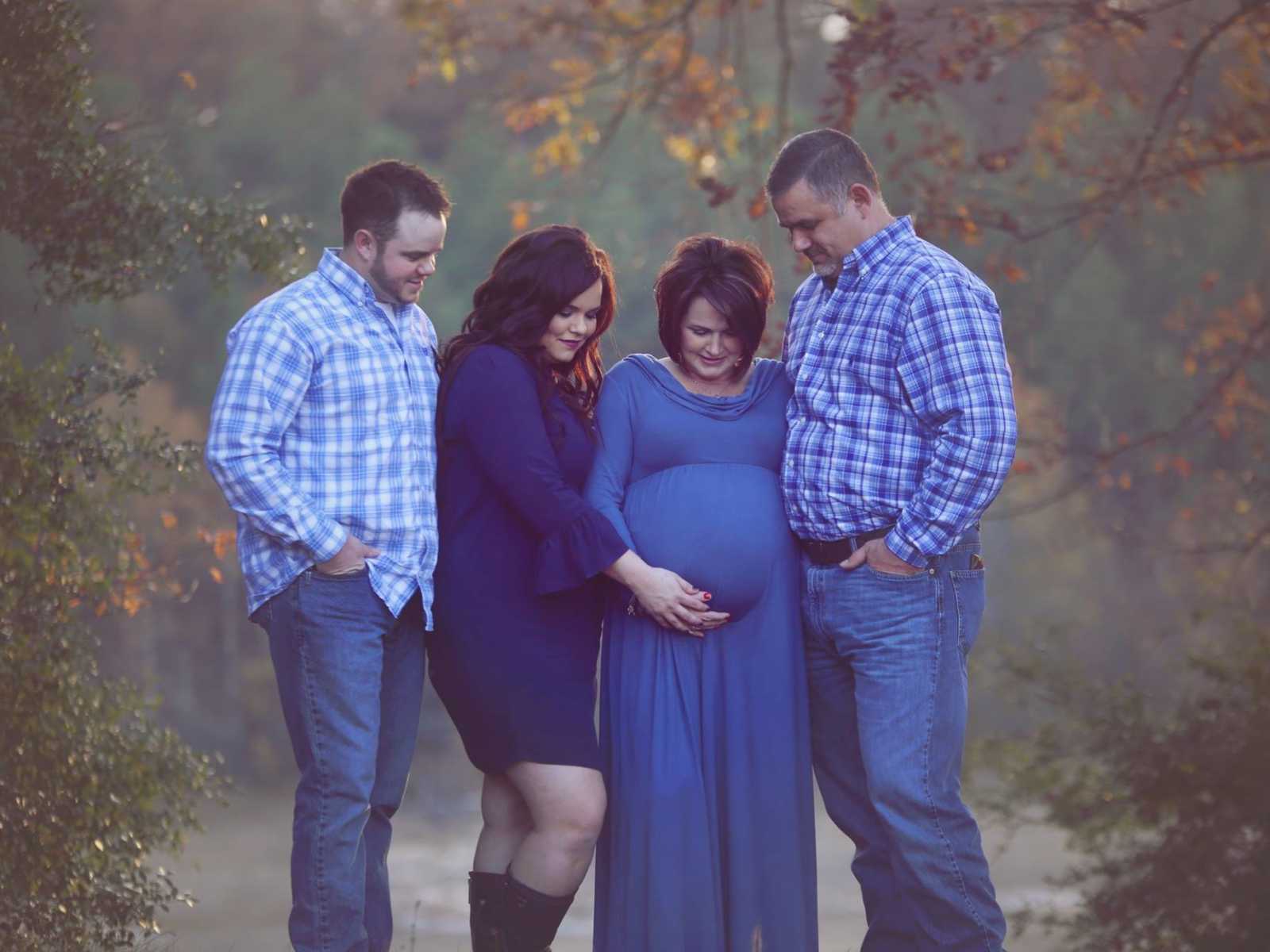 two couples stand next to each other and the two woman have their hands on the pregnant stomach