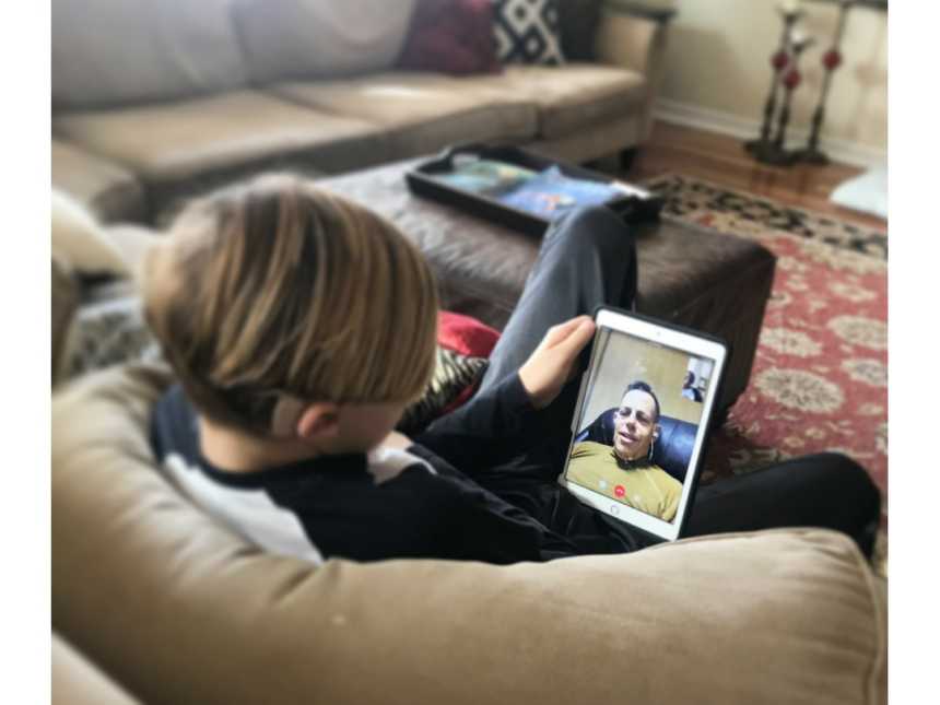 Son sits on couch on facetime with deployed marine father