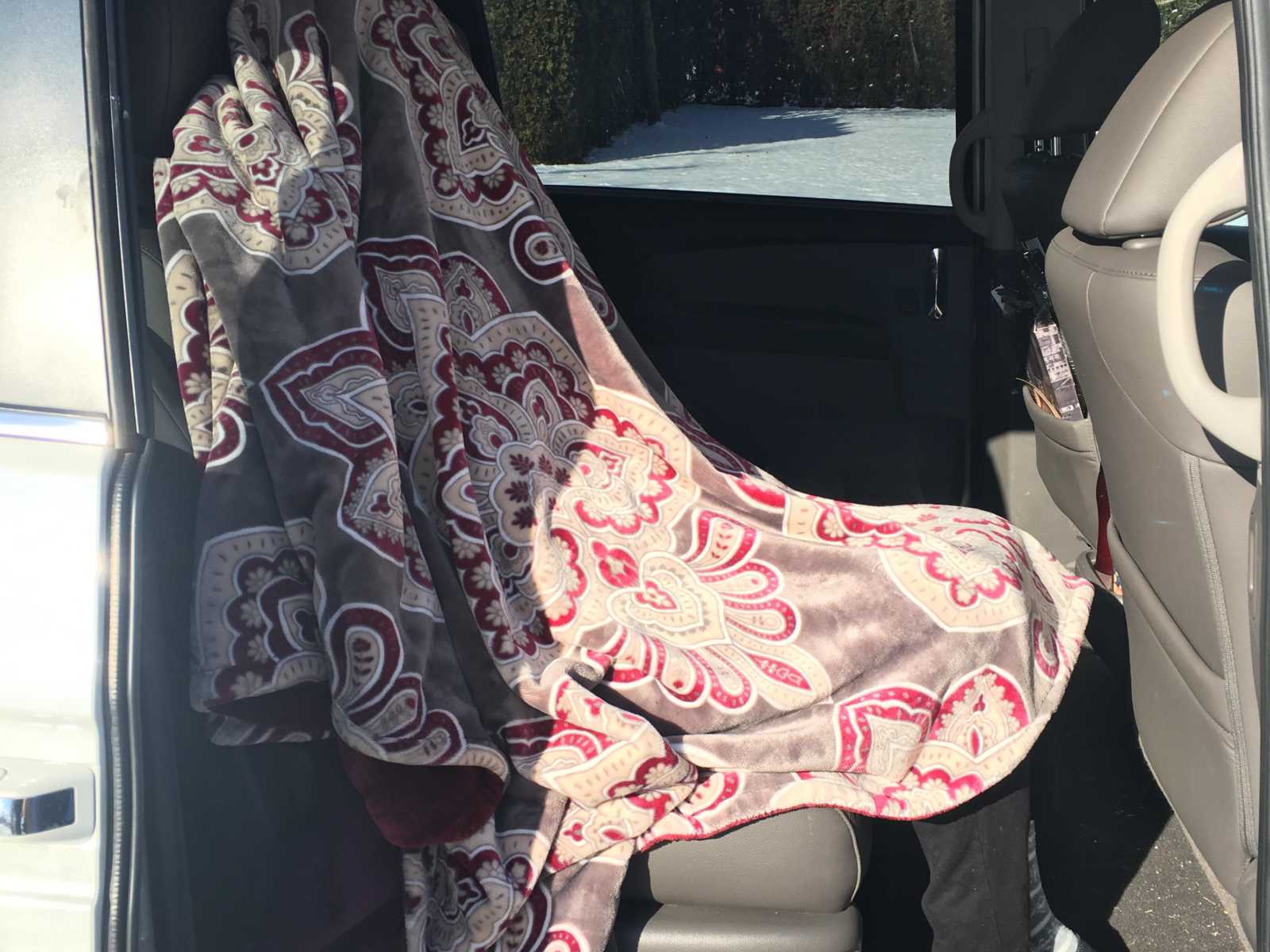 View from outside the car door of woman with dementia sitting in backseat with blanket over her head