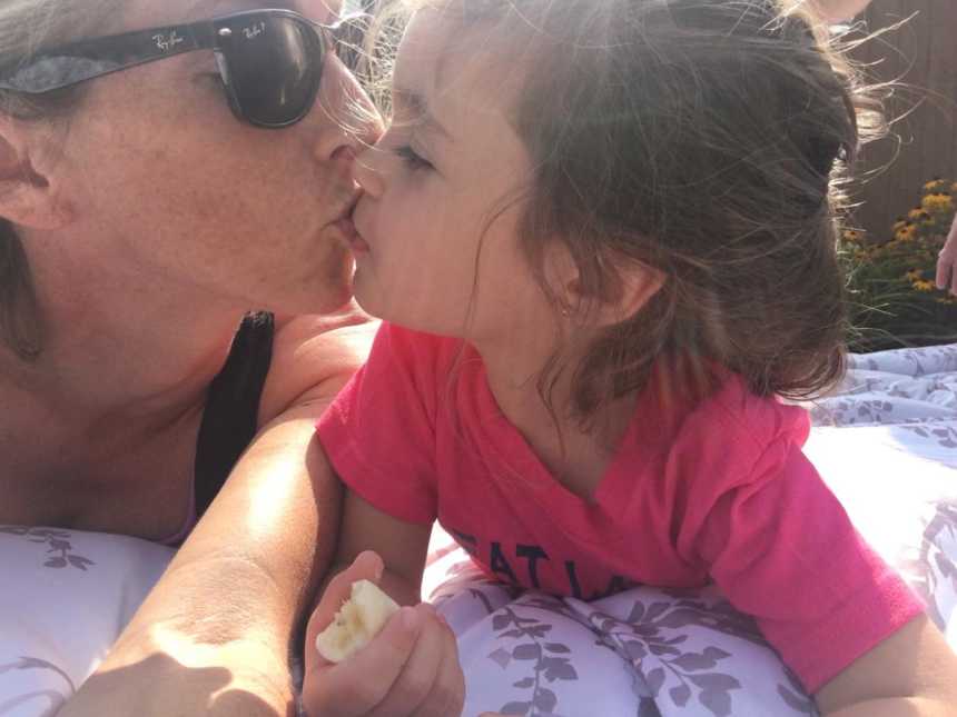 mother wearing sunglasses takes selfie of she and her daughter kissing