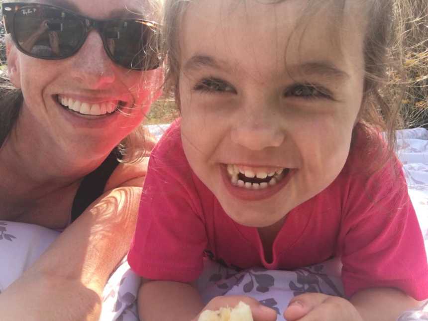 mother wearing sunglasses takes selfie with daughter laying down 