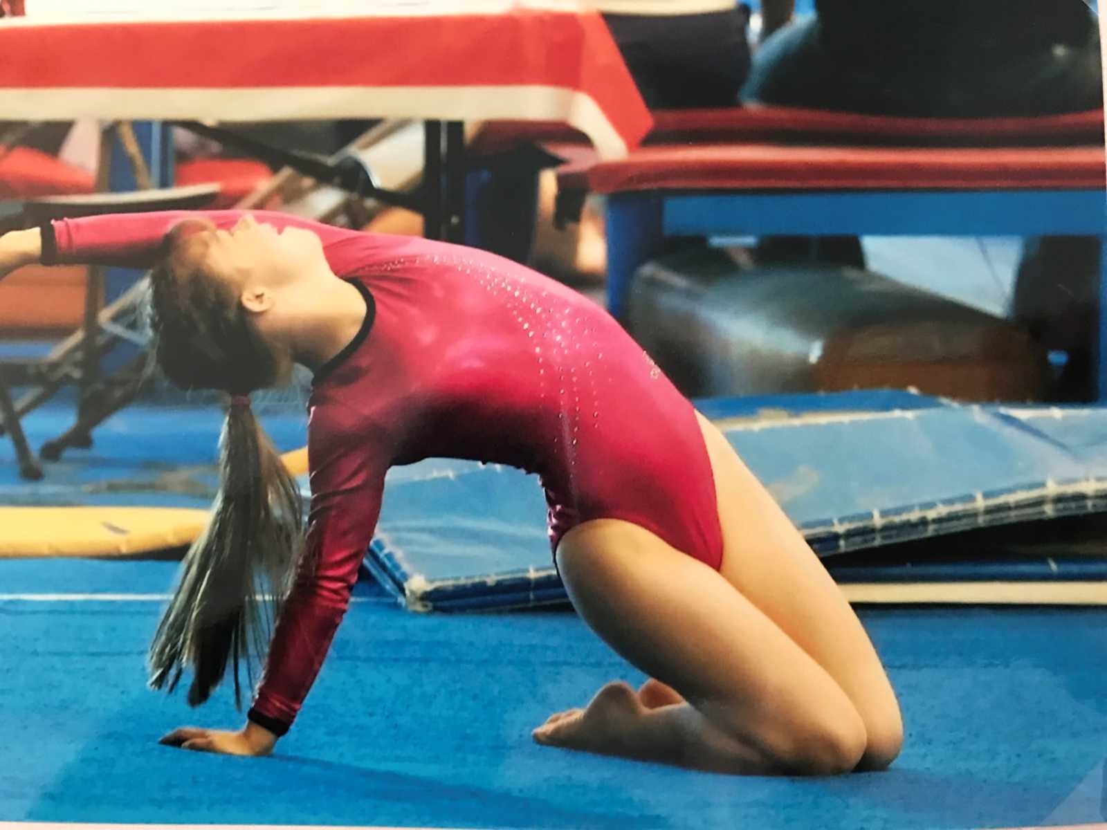 down syndrome girl in pink sparkly leotard poses on the floor doing gymnastics