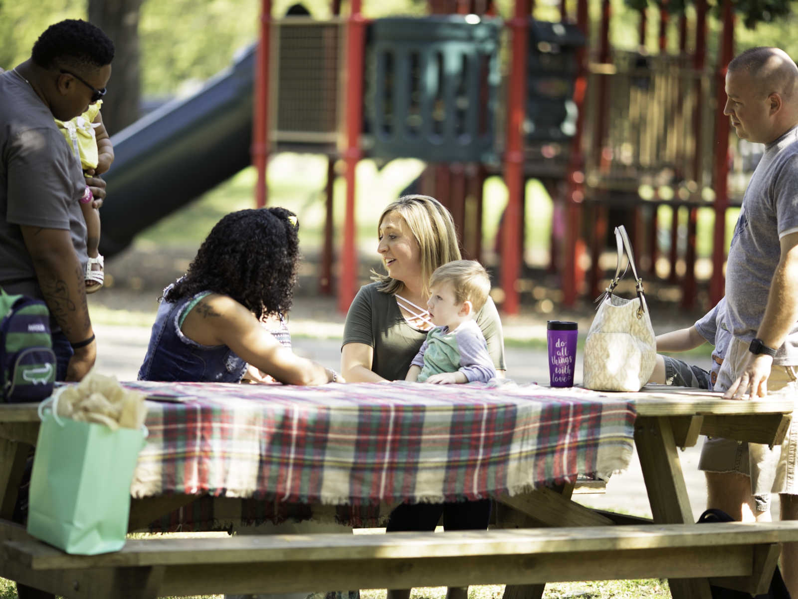 families sit down to talk at picnic table at a playground