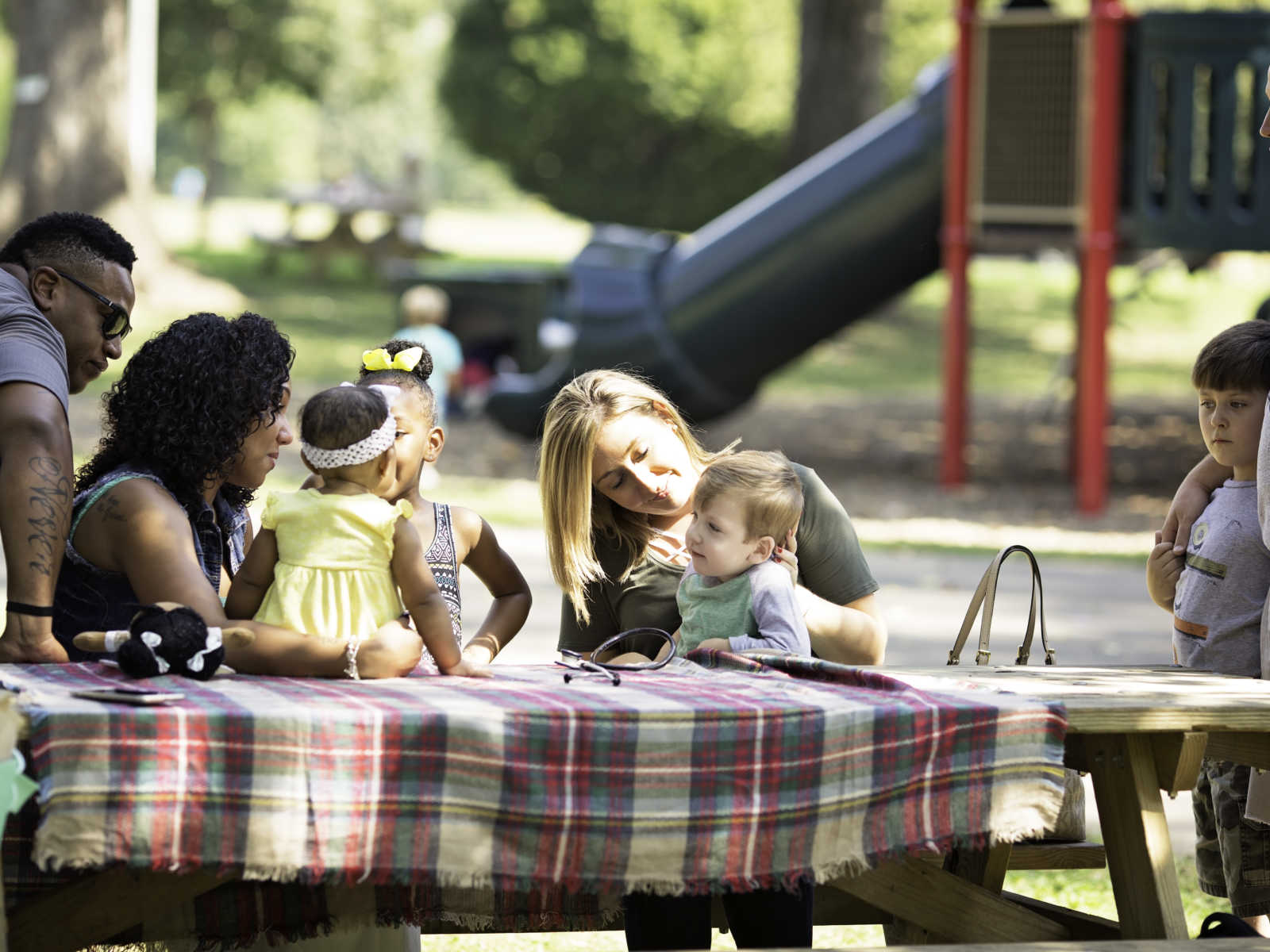 Two families sit at picnic table at playground