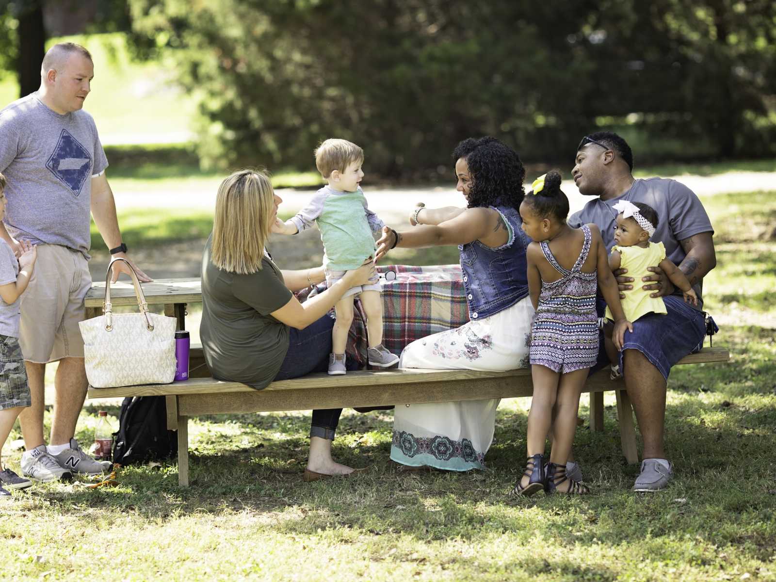 Woman sits at picnic table holding arms out for little boy who has her daughters heart to hug her