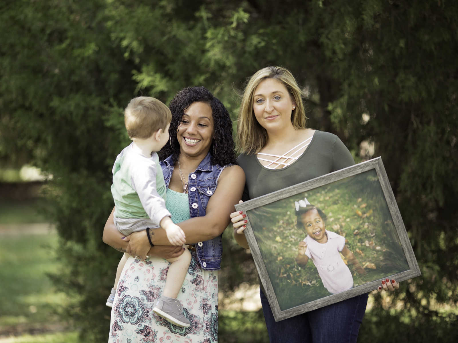 Woman holds little boy beside his mother who holds picture of deceased little girl