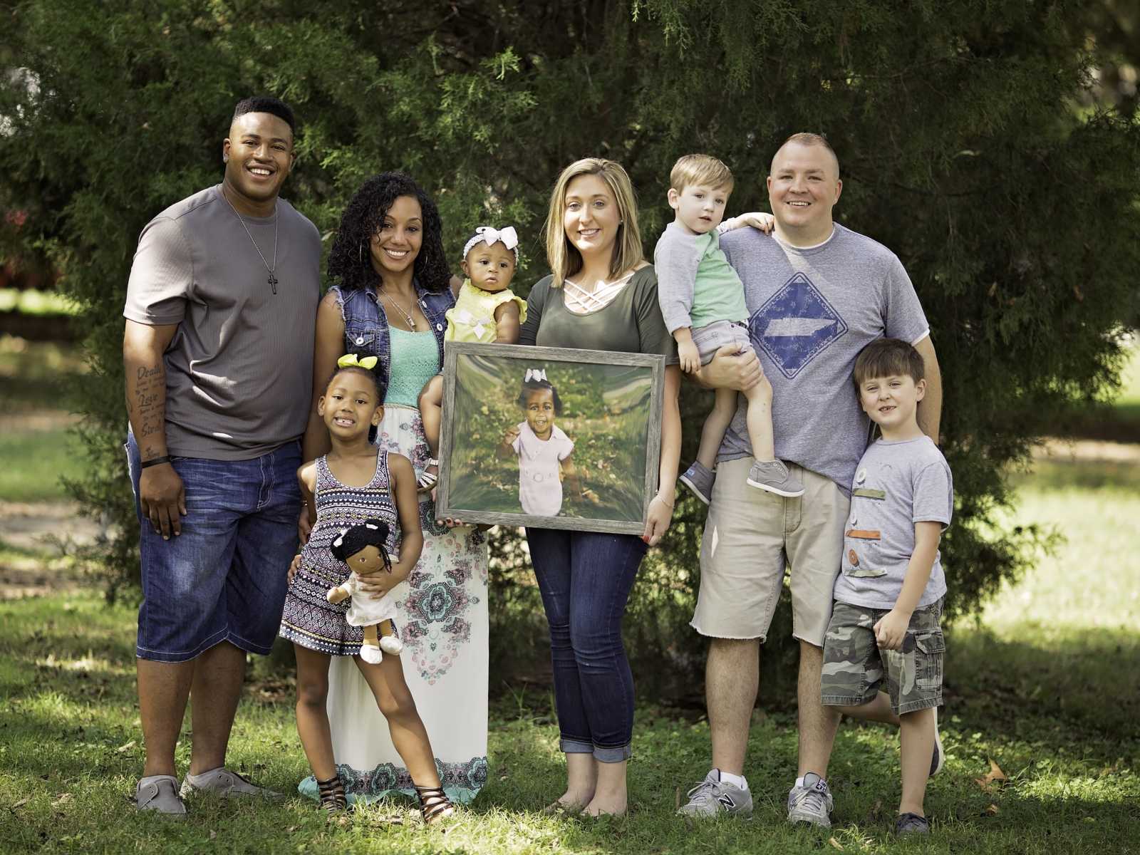 Two families stand outside while one mother holds frame of other mother's deceased daughter