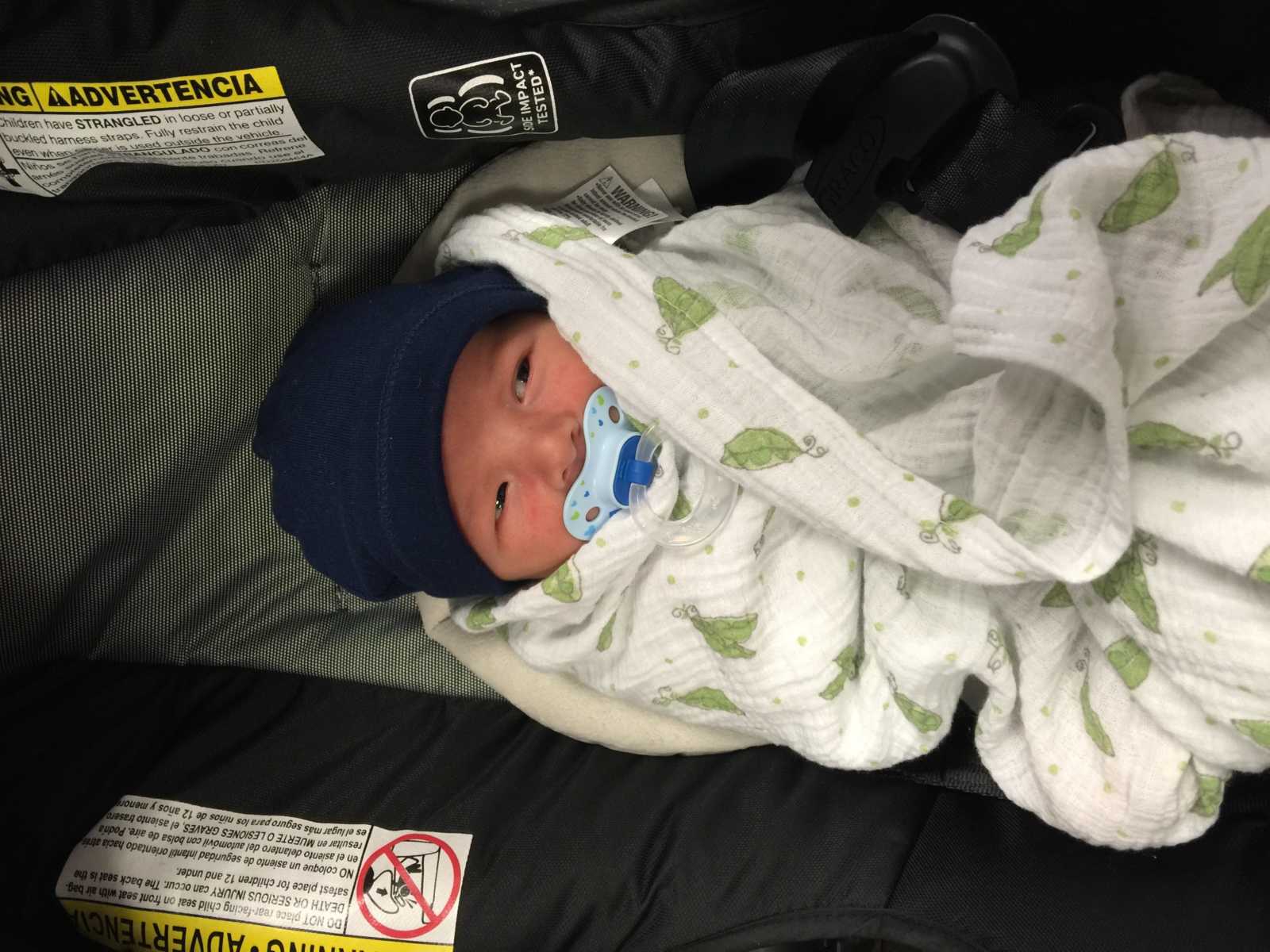 baby wrapped in blanket with pacifier and hat on 