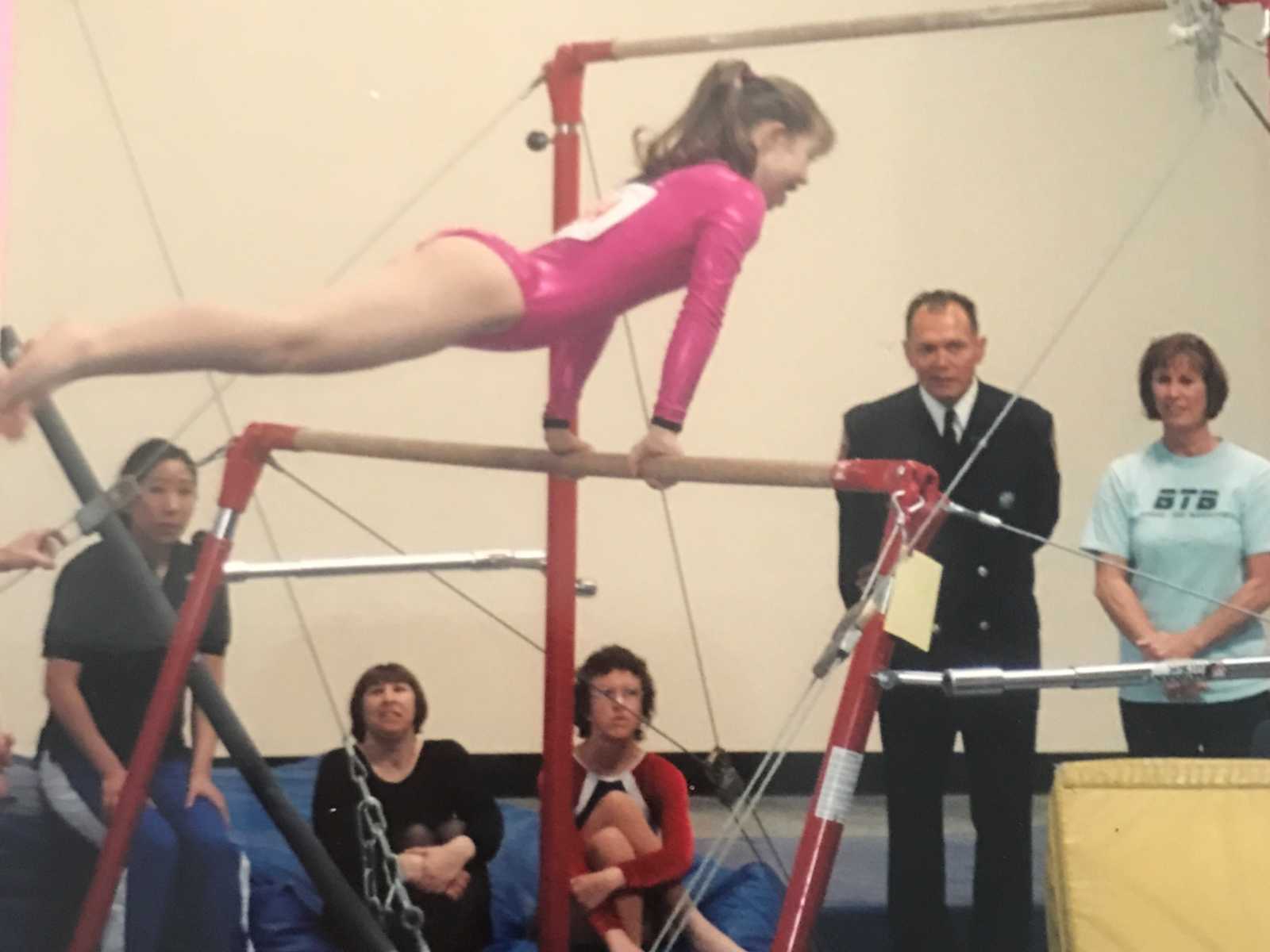 down syndrome girl in sparkly pink leotard at gymnastics competition on the uneven bars with people watching