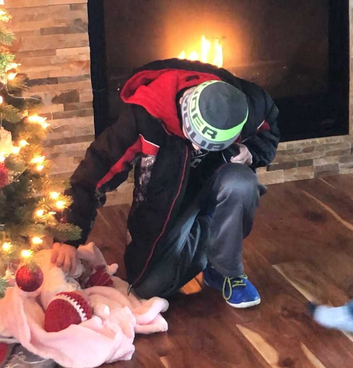 young boy kneels and touches adoptive sister lying under the Christmas tree