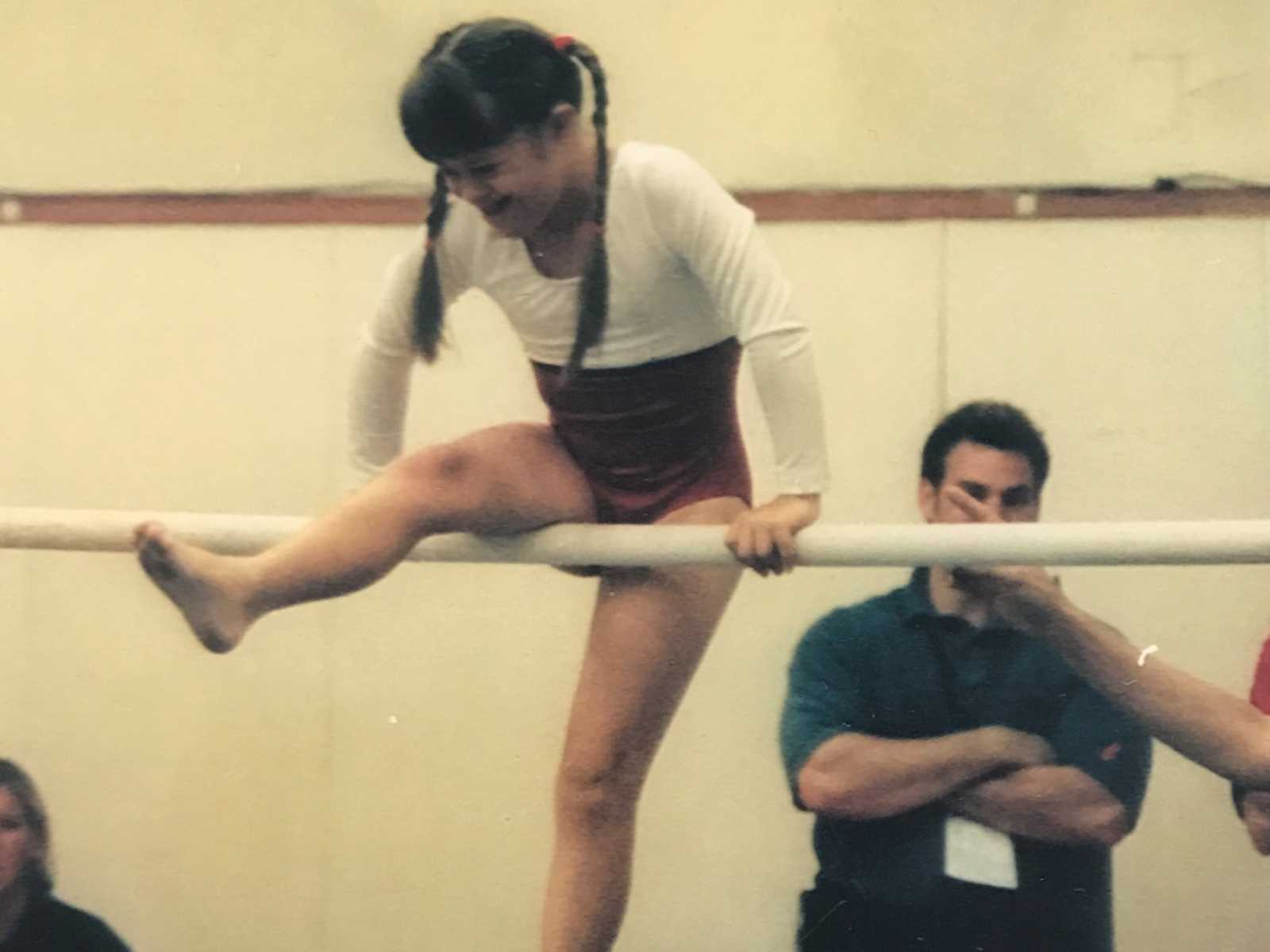 down syndrome child with braids wearing leotard on a gymnastics bar with a man close by for support