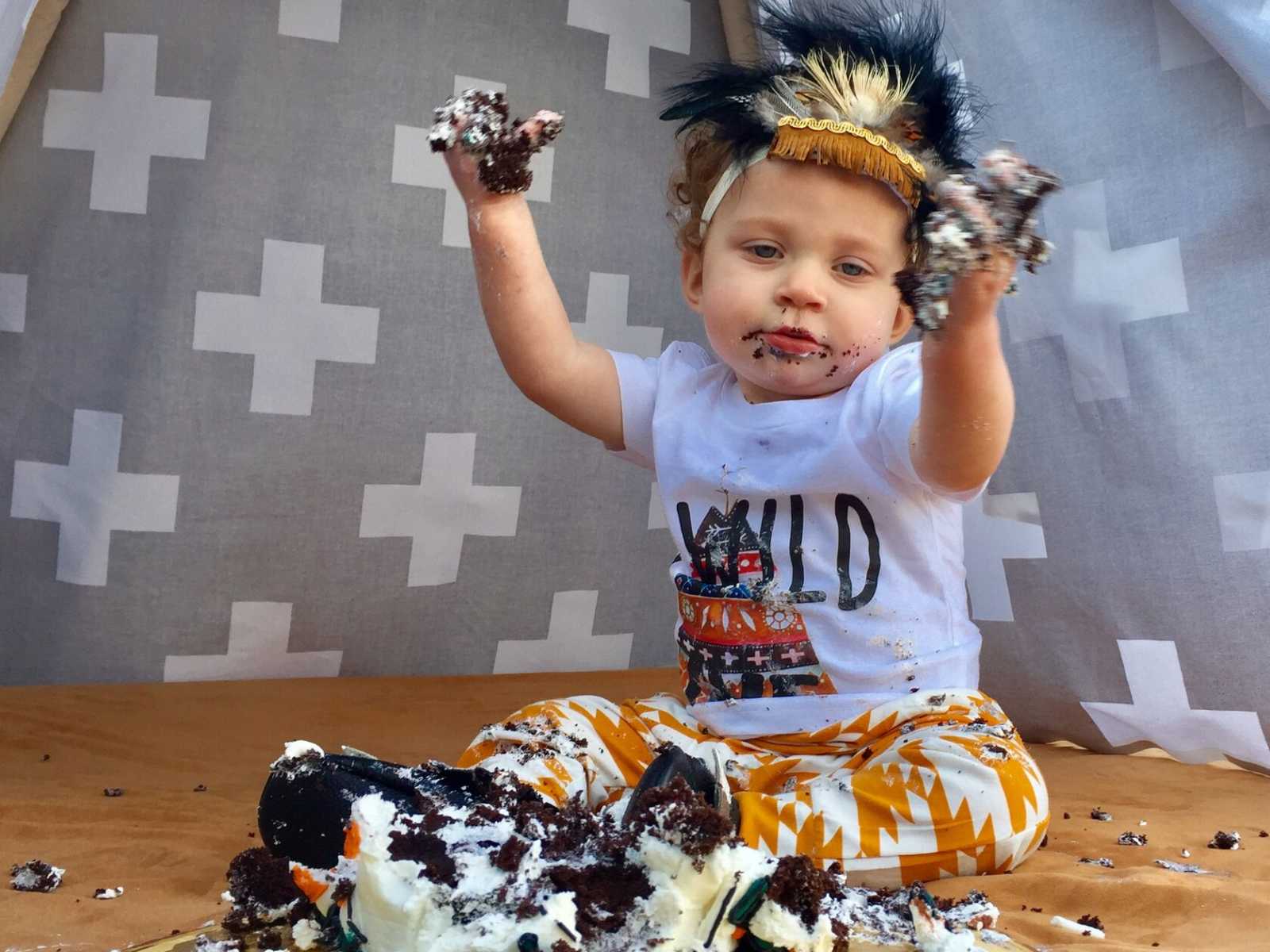 adopted toddler sitting with a destroyed cake in front of him that all over his hands and face