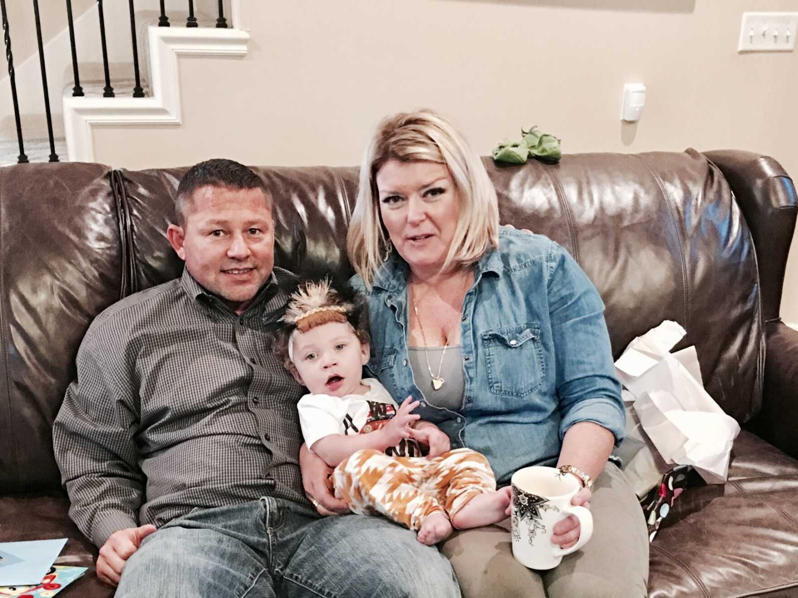 mother and father sit on brown leather couch with adopted son in their lap