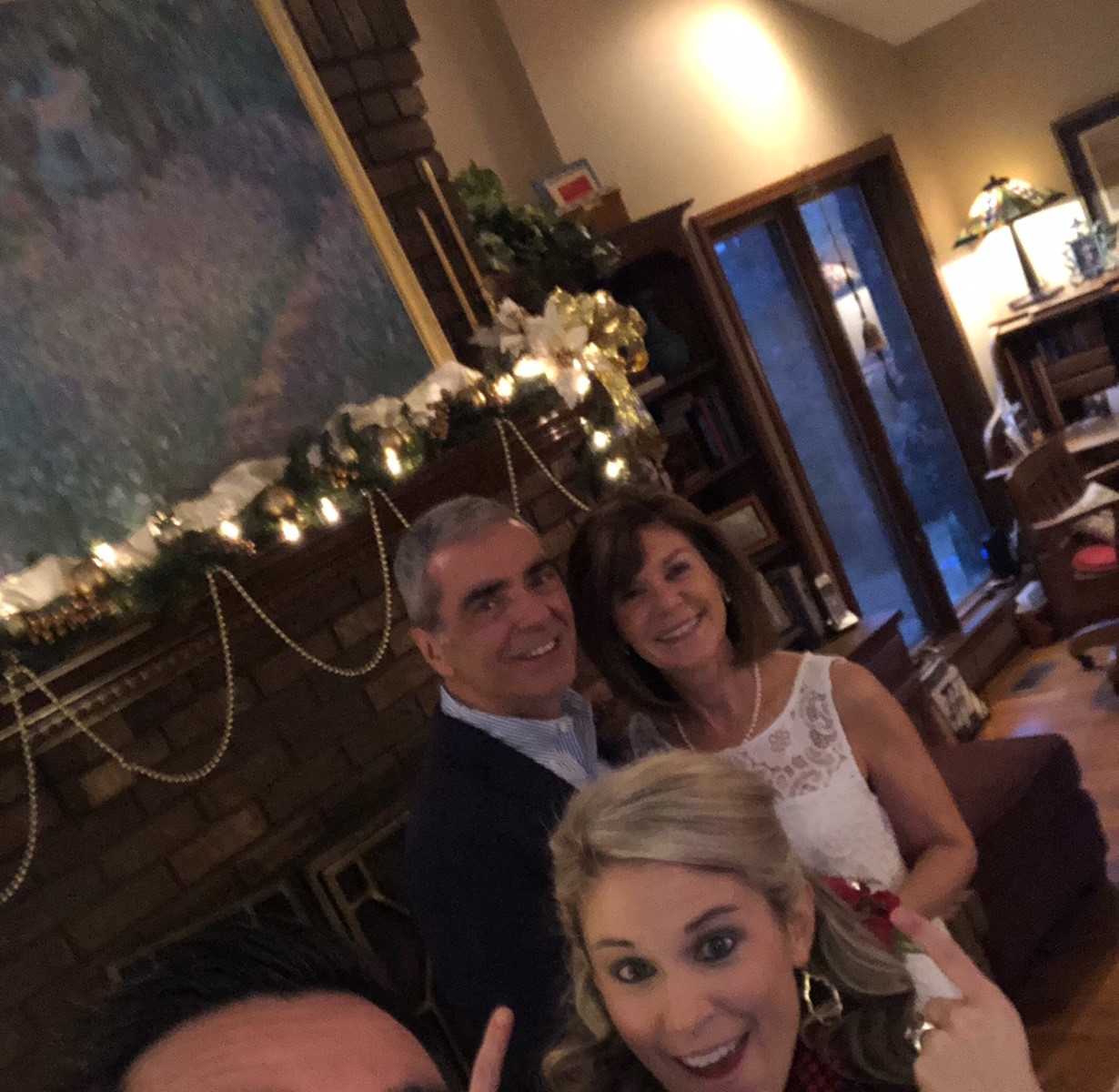 man takes selfie with a woman and couple smiling int the background in front of a fire place