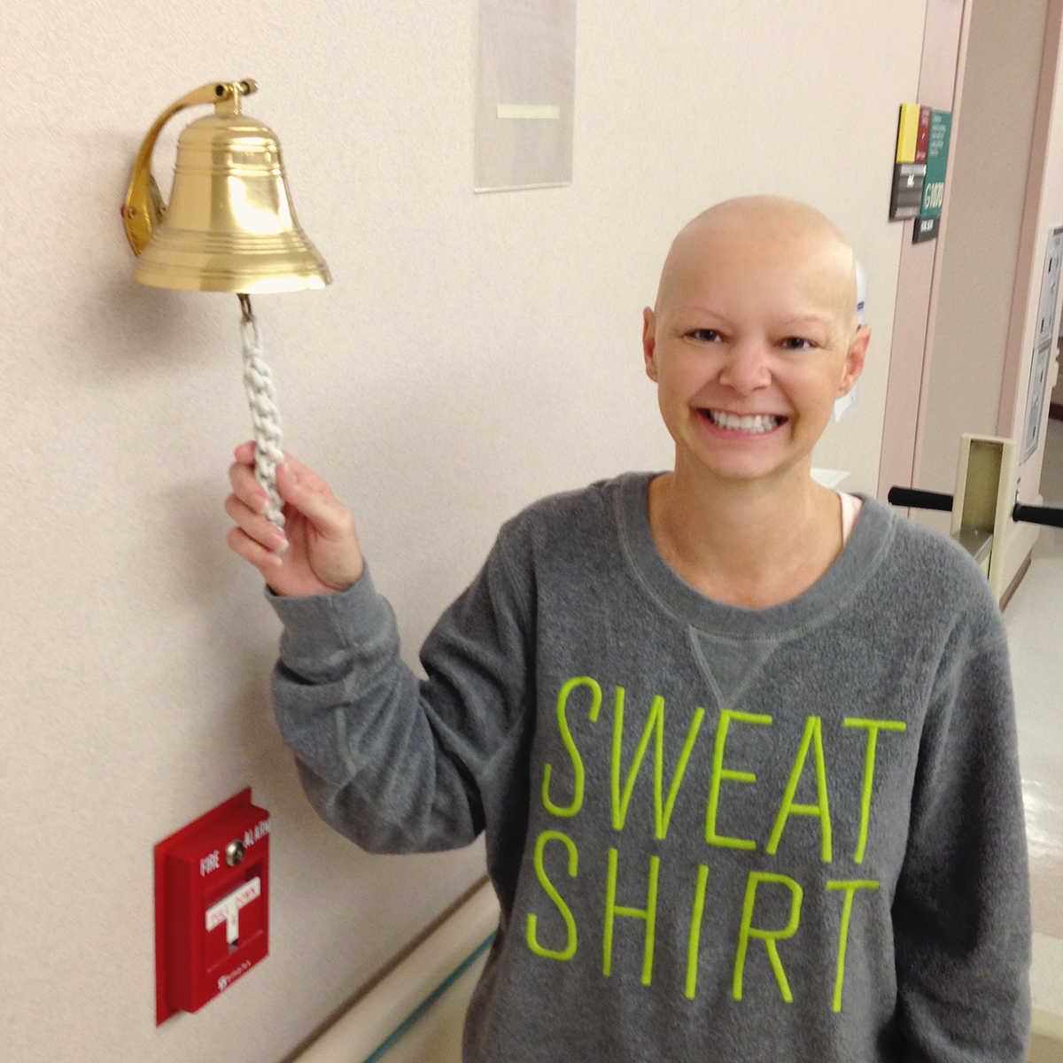 woman with cancer smiling and ringing a cold bell in hospital hallway