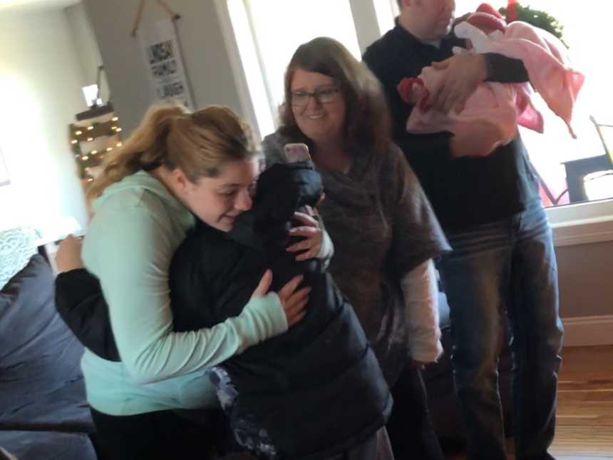 son hugs his adopted sisters birth mom while mom takes a photo and dad holds baby
