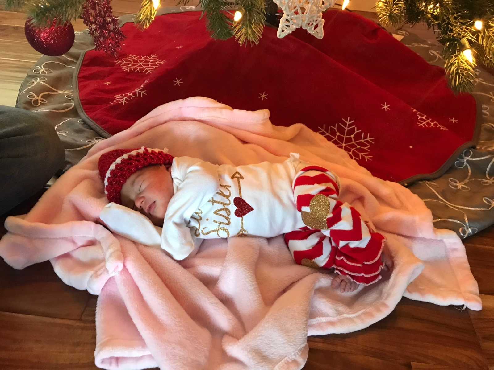 newborn baby girl lying under Christmas tree in pink blanket with shirt saying sister on it