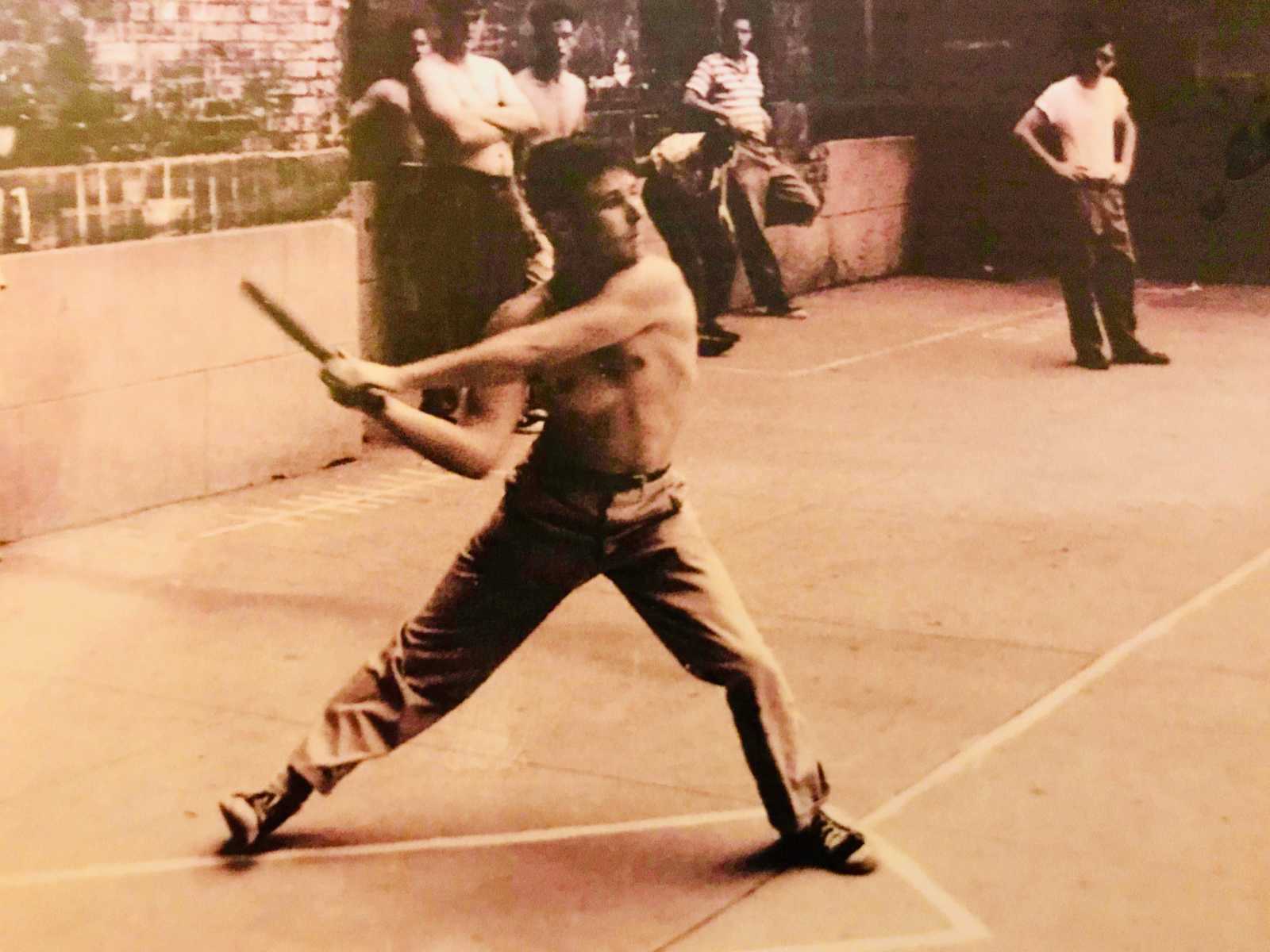 Shirtless teen in 20s swinging baseball bat