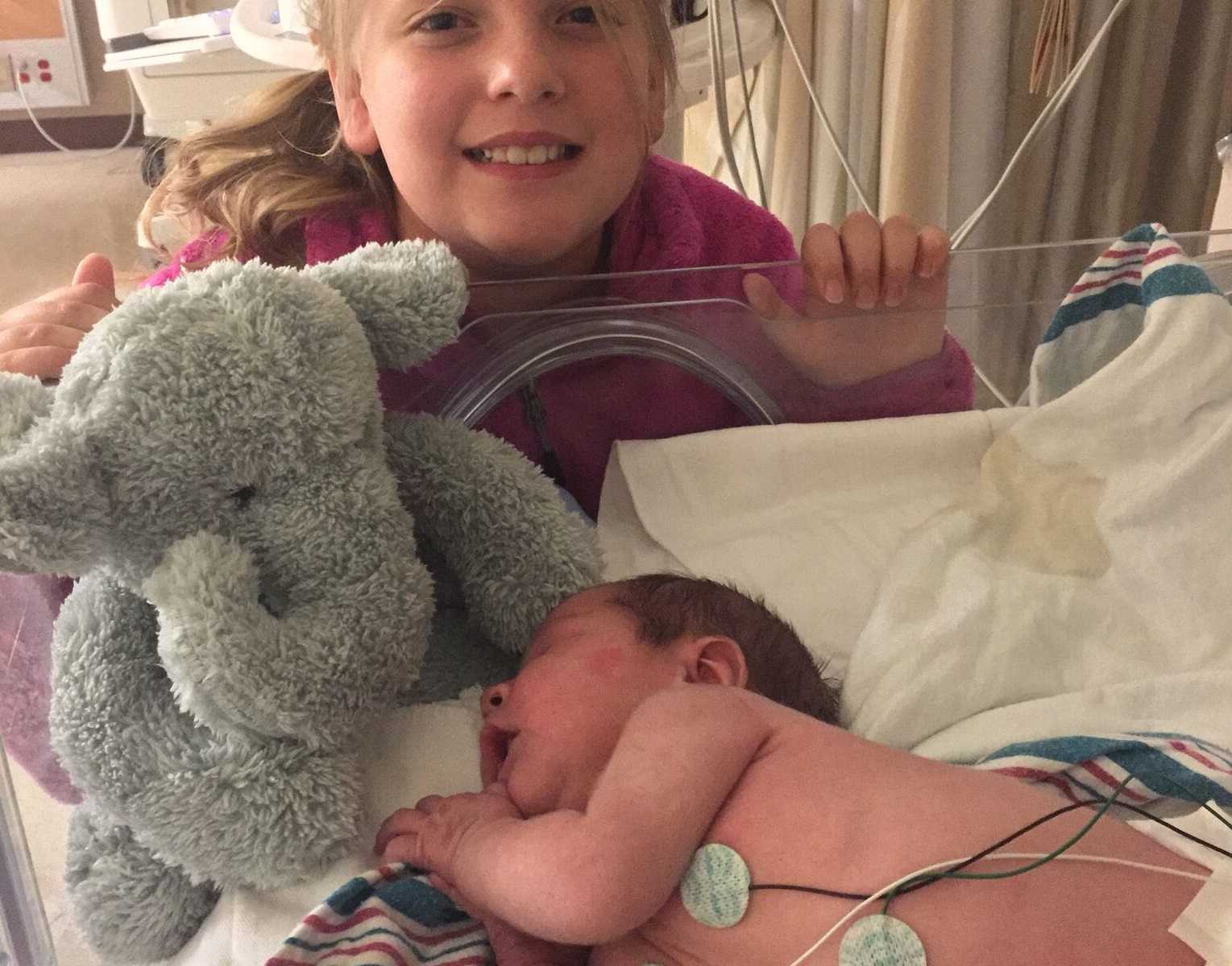 older sister leaning next to adopted brother sleeping at hospital with an elephant stuffed animal