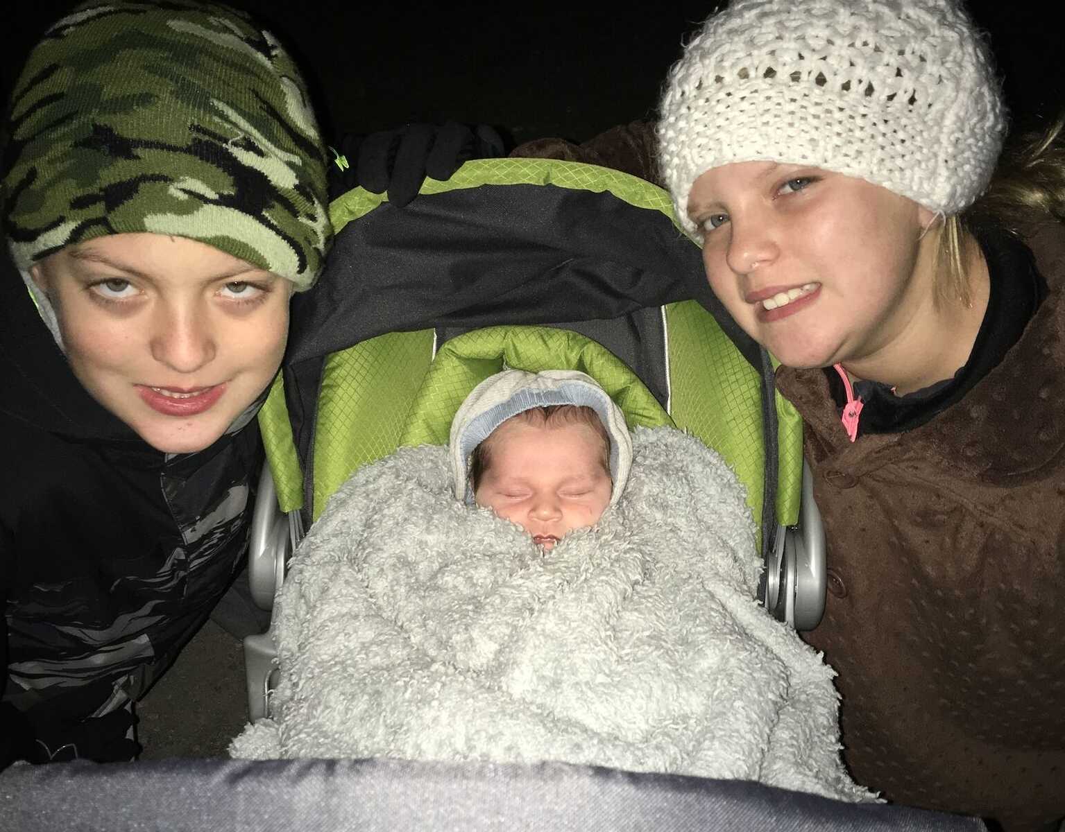 older brother and sister smiling next to adopted baby brother sleeping in a stroller 