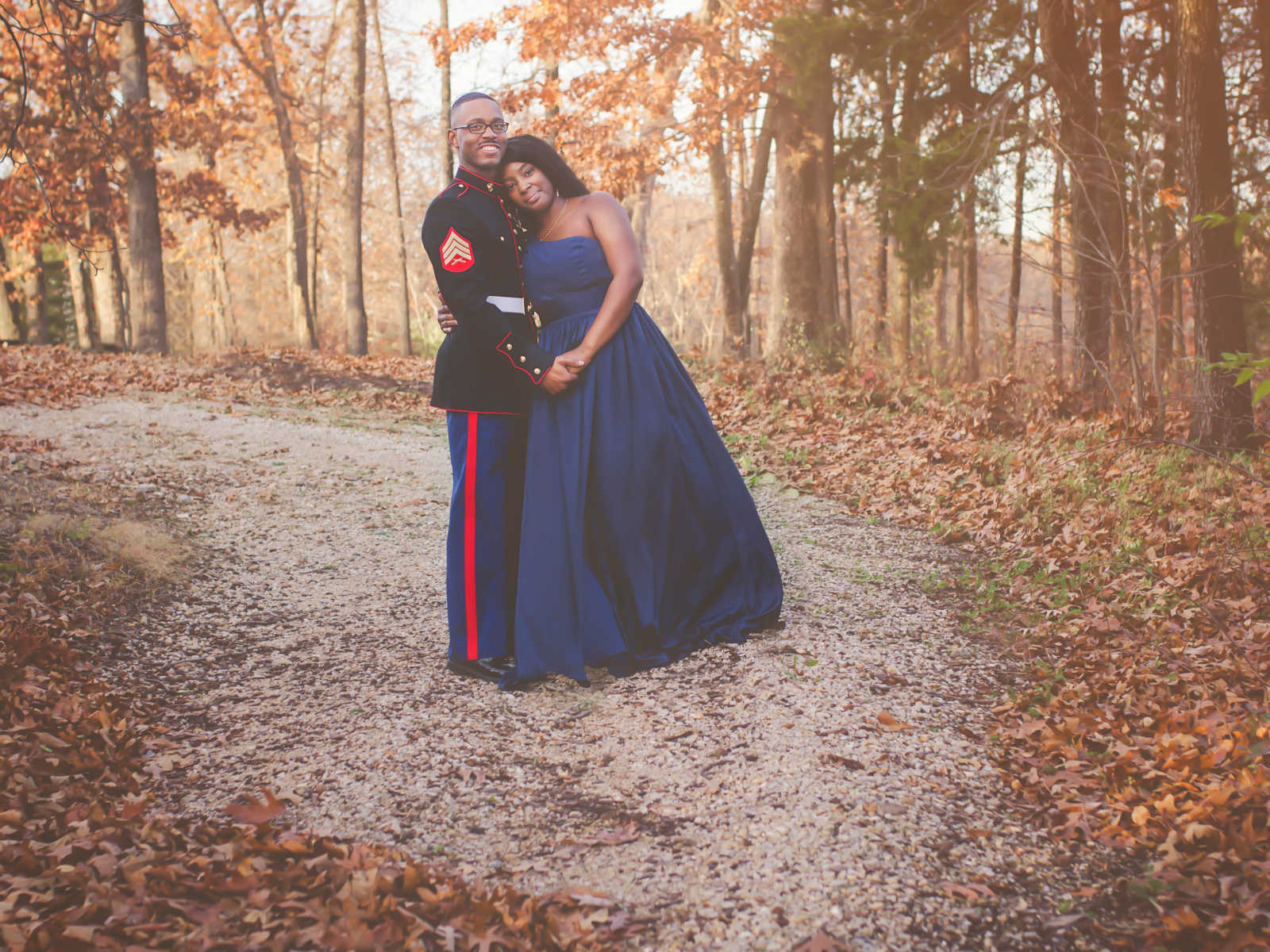 marine husband holds wife in his arms as she wears a blue strapless gown in a trail in forest