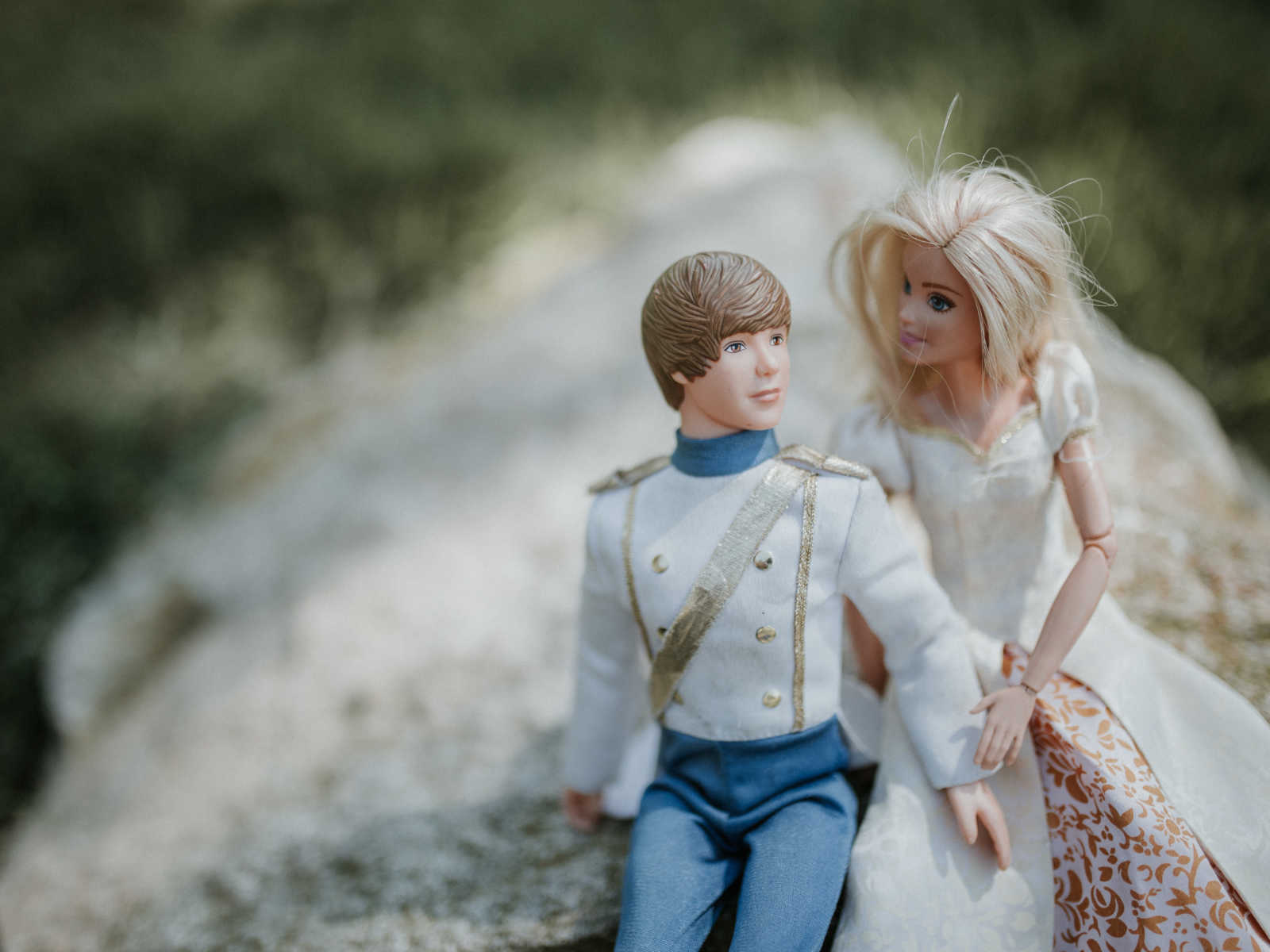 barbie looks at ken while sitting on a rock and holding hands
