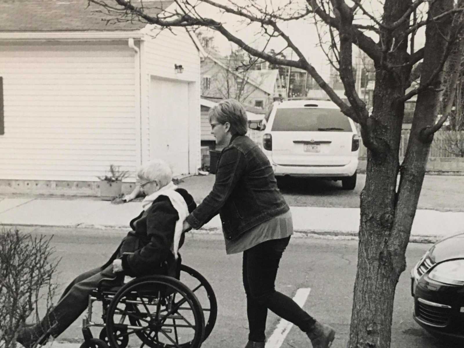 Woman pushing woman in dementia in a wheel chair on the sidewalk