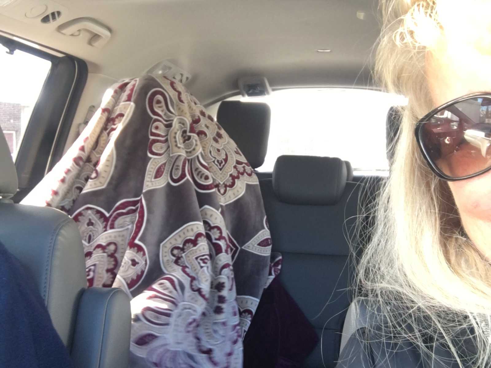 Woman in front seat of car takes selfie of mother with dementia in the backseat with blanket over her head