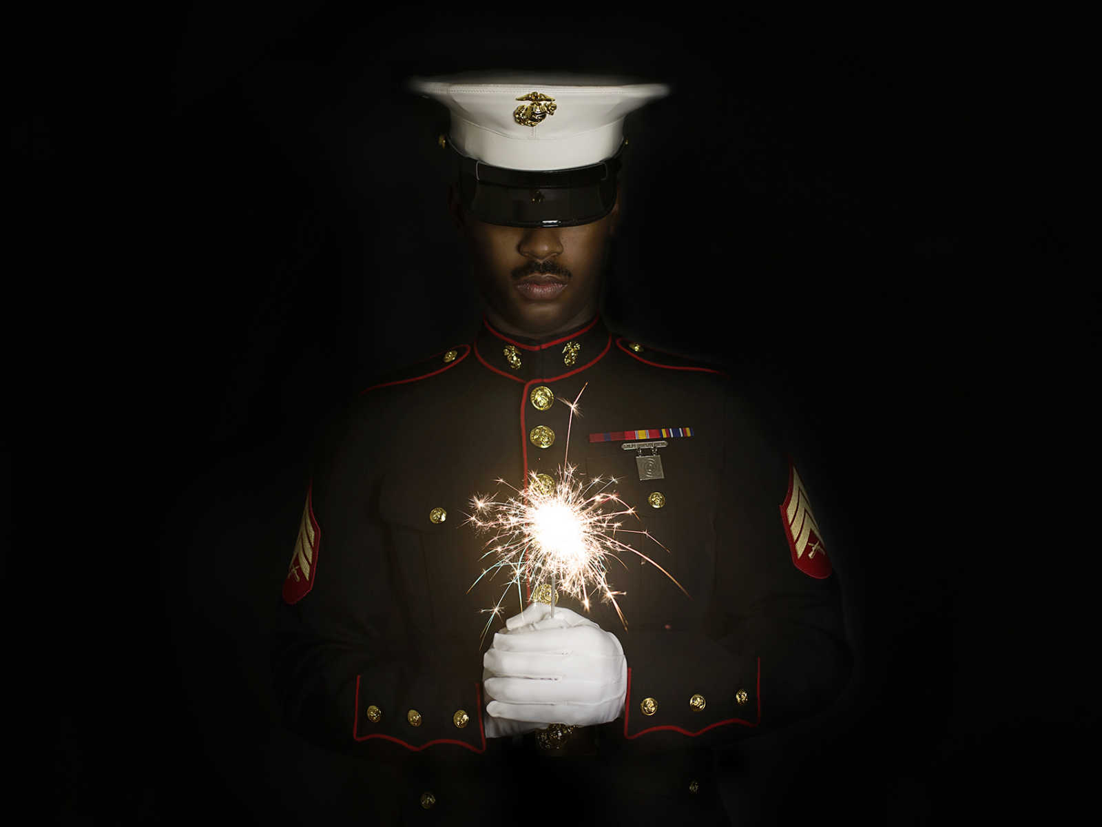 marine husband is in uniform holding a sparkler which is the only thing lighting up his face