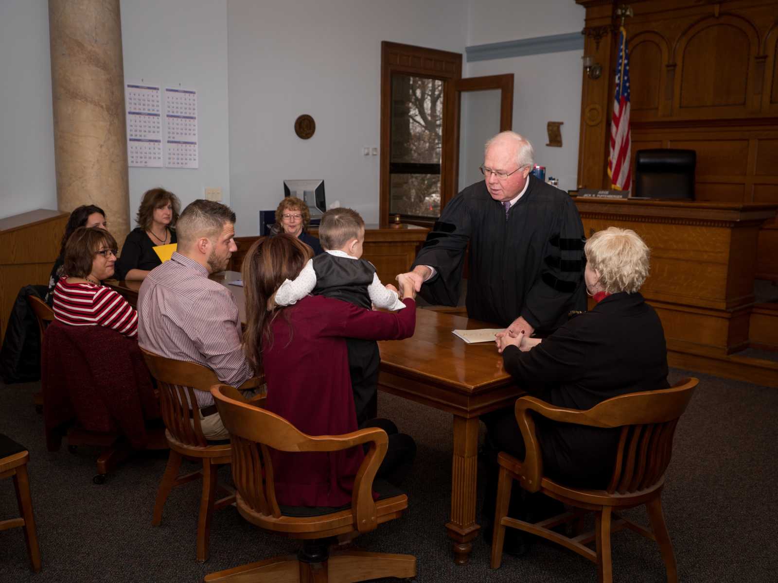 judge shakes hand of adoptive child who is at table with his parents and others