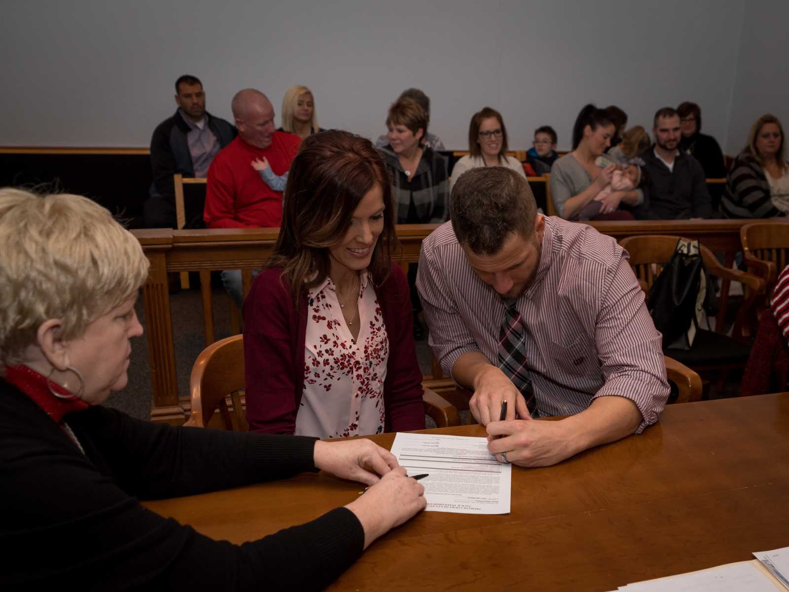 couple signs papers at adoption court with happy crowd looking on