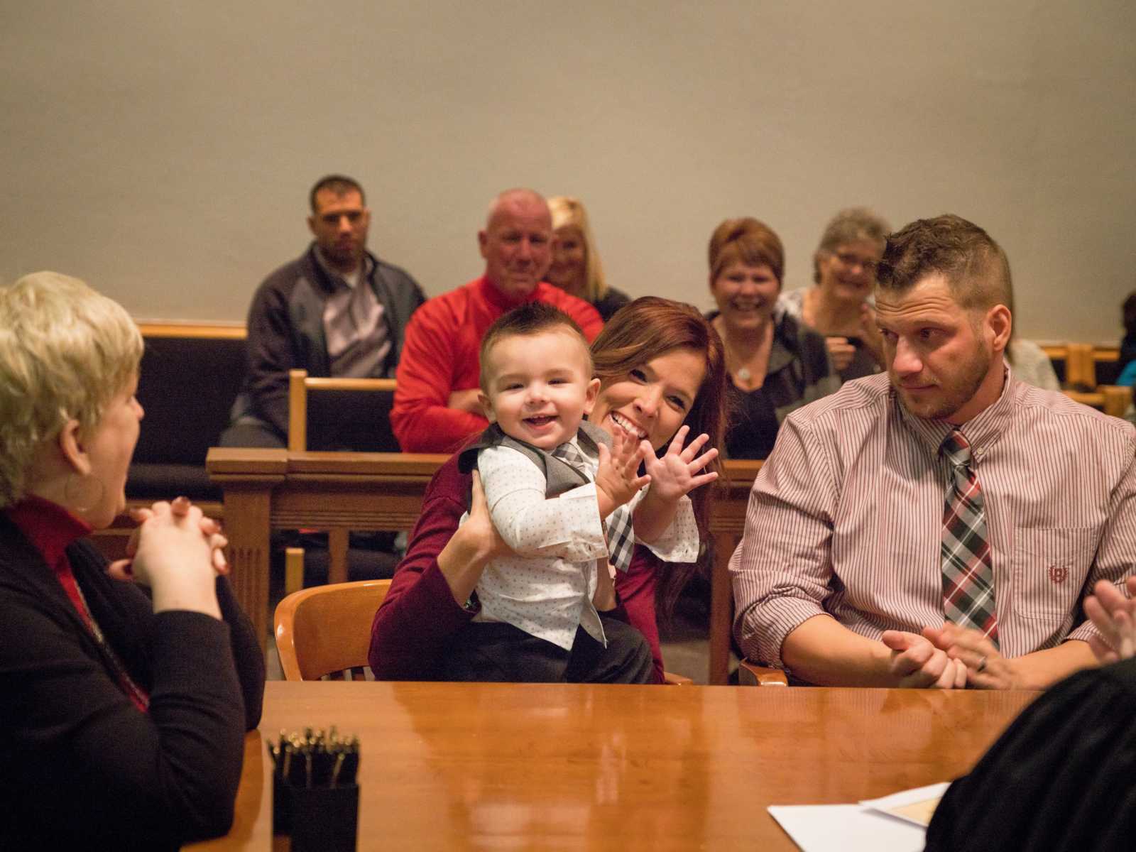 adoptive child is cheering in mothers lap as the crowd smiles