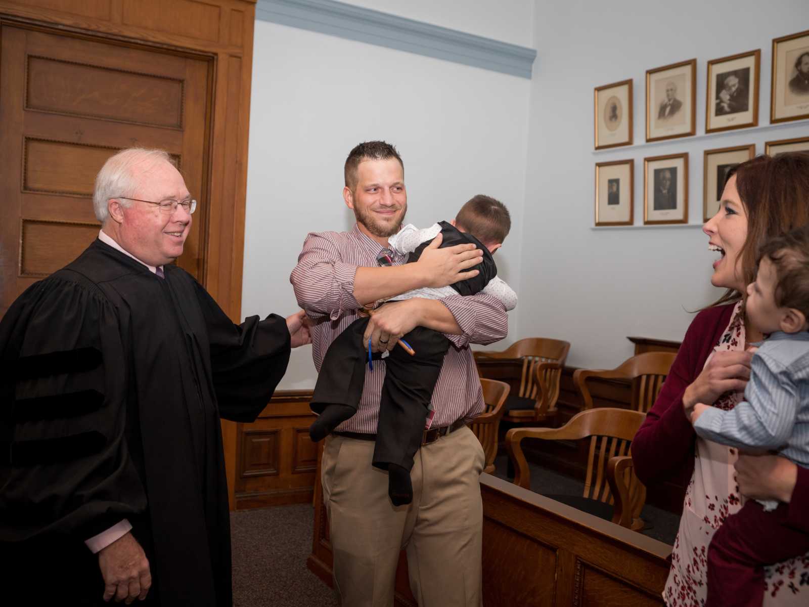 judge smiling at adoptive parents as father holds his son and wife holds other child
