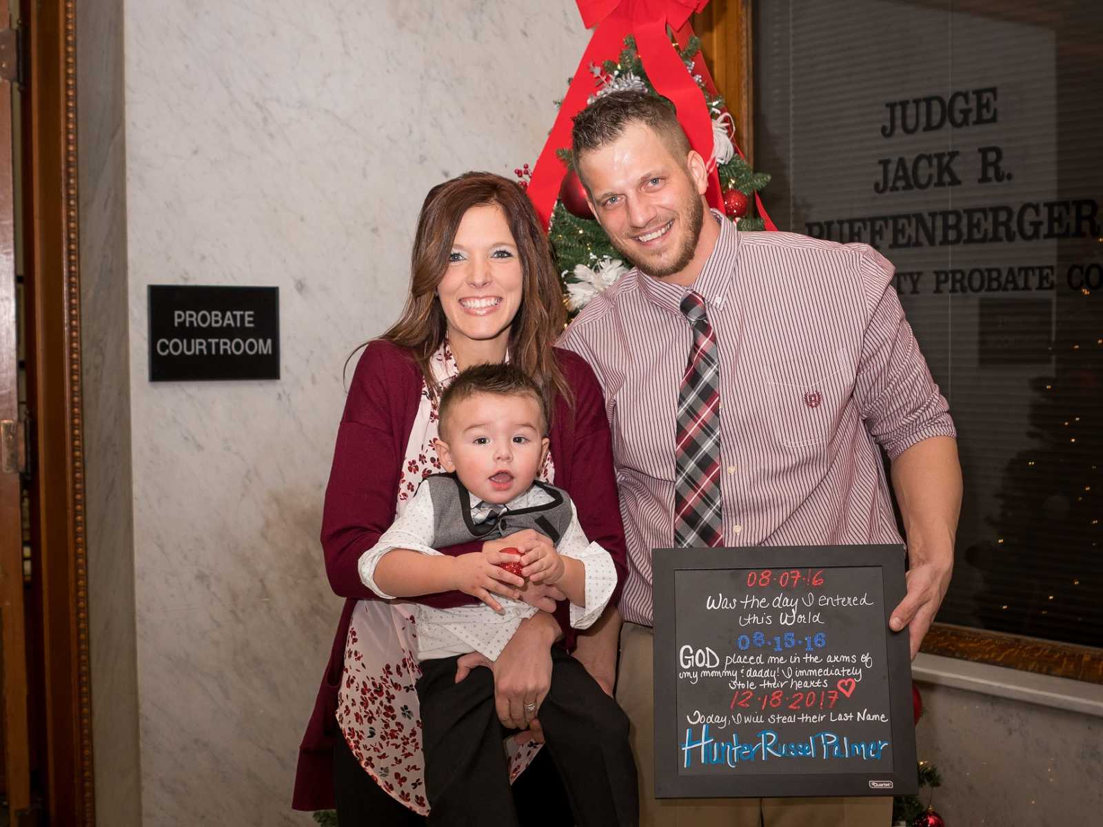 adoptive parents pose for picture with adoptive son and sign with the date of the adoption and childs name