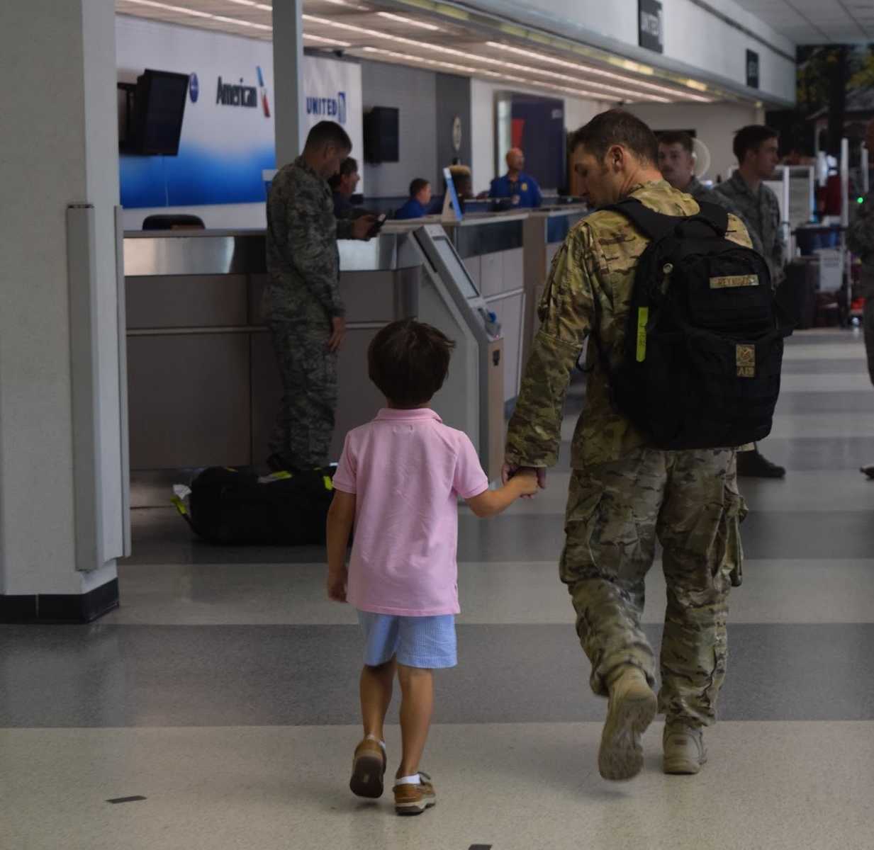 soldier in camo holds hands with son while walking to check in desk at airport