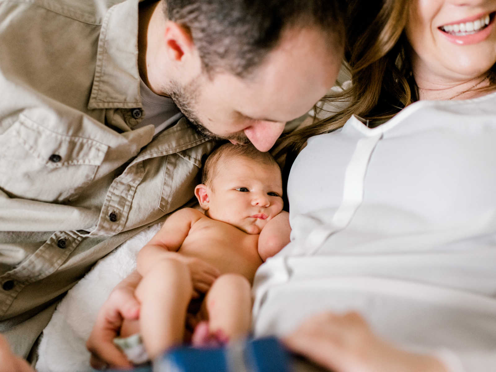 father leaning over to kiss baby that is being held in mothers arms