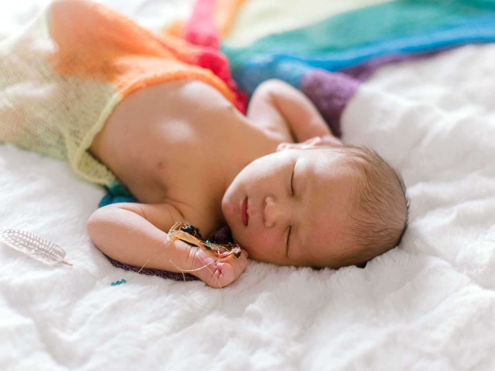 baby sleeping on a blanket that looks like a rainbow with toy in hand